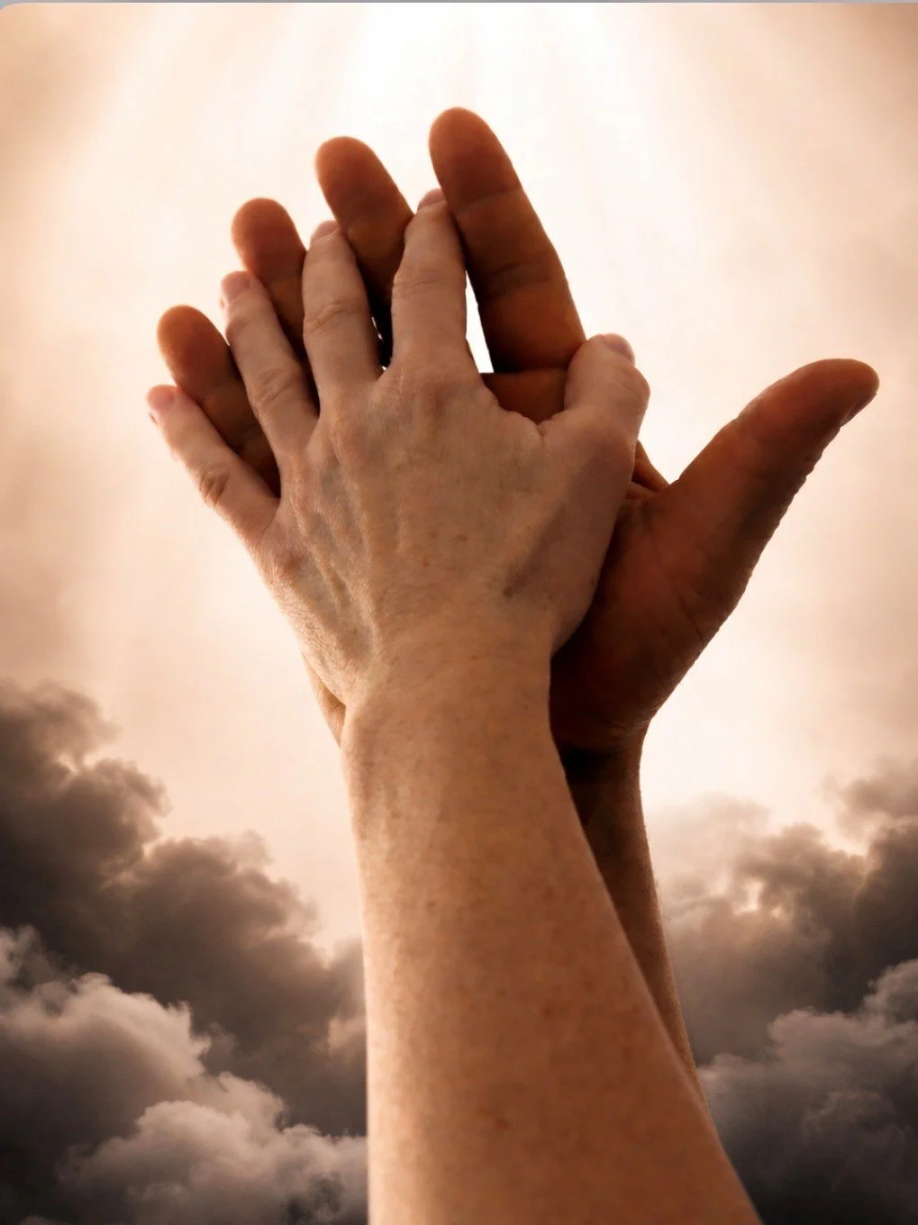 Two hands, one older and one younger, clasped together against a cloudy sky background.