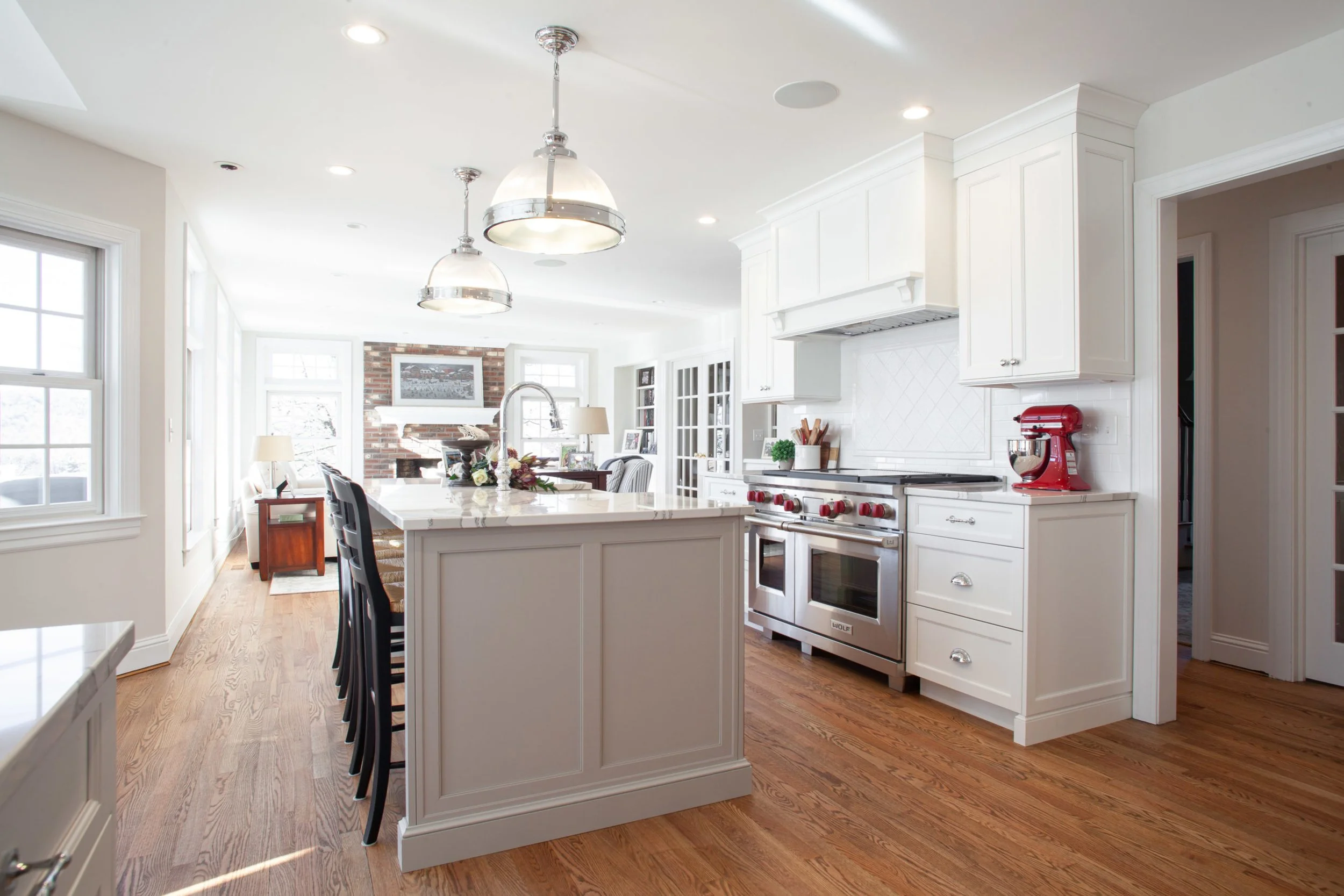 Bright kitchen with white cabinets, a large island with barstools, stainless steel oven and stove, red stand mixer, and natural light from multiple windows.