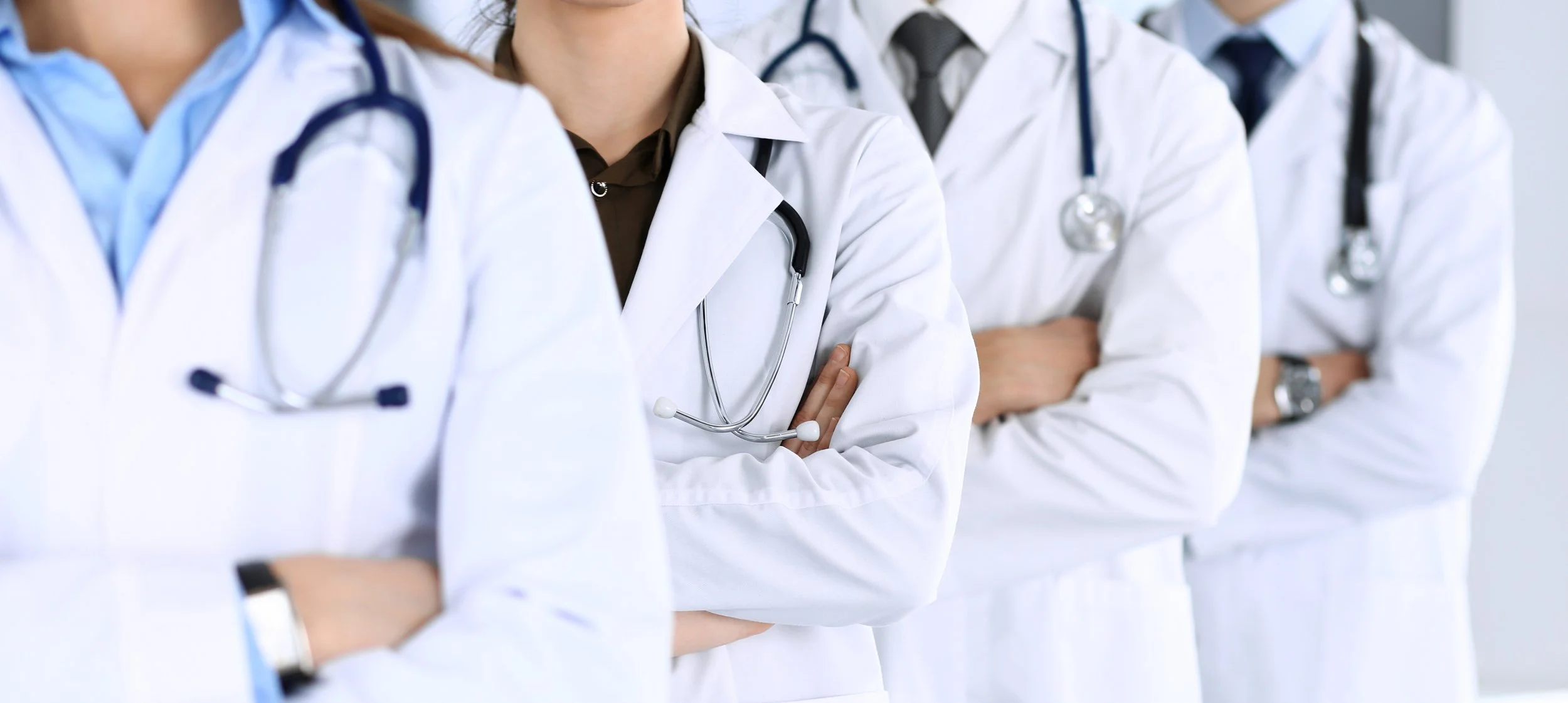 A group of medical professionals wearing white coats and stethoscopes around their necks standing with arms crossed.