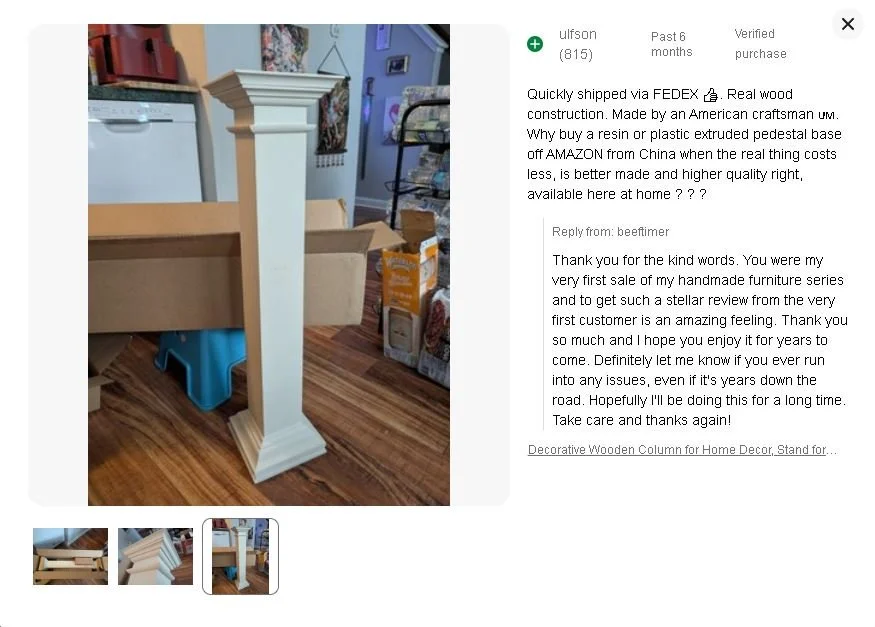 A decorative white wooden column with a square base and ornate molding at the top, standing on a polished wooden floor in an indoor setting.