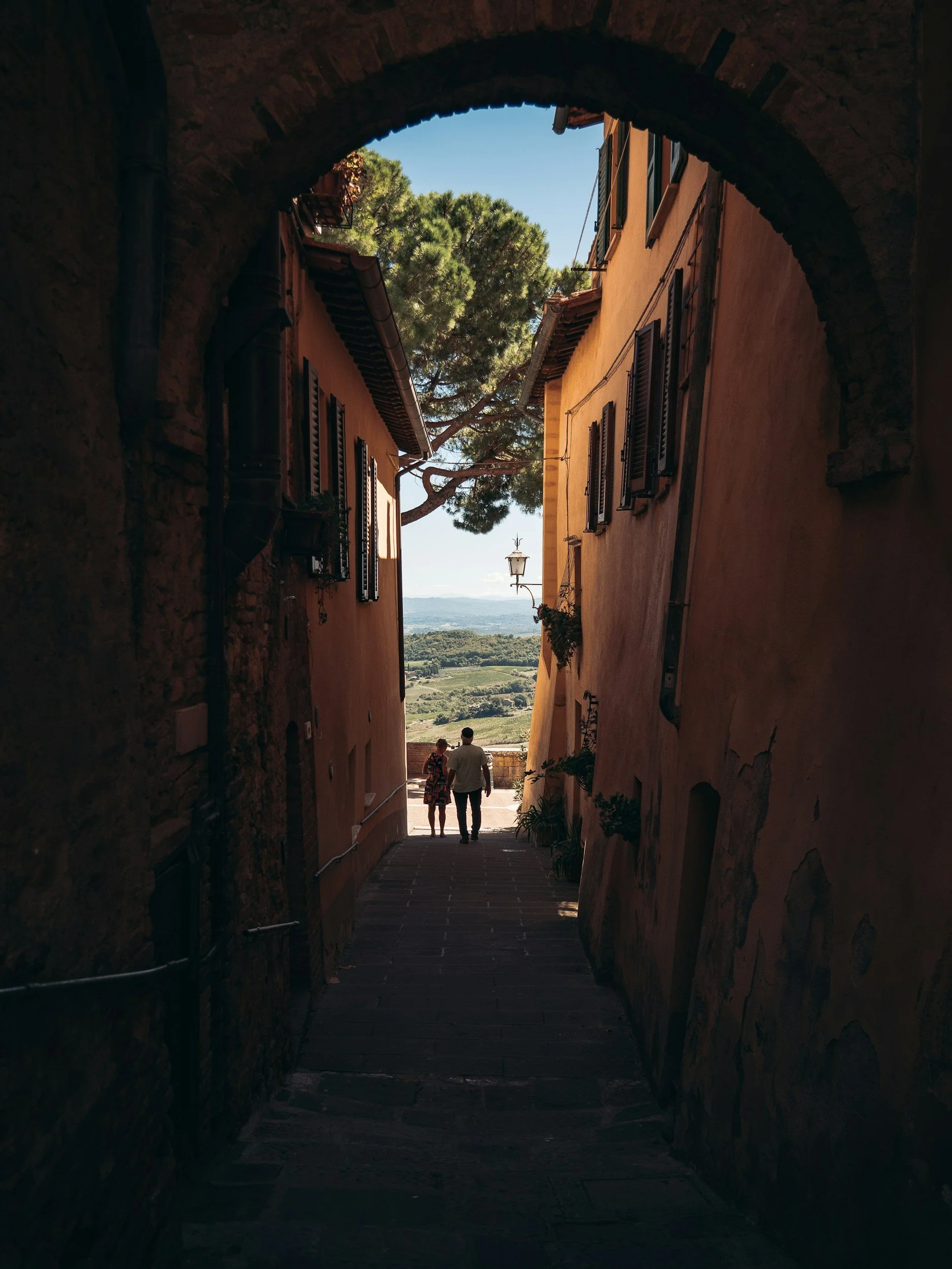 couple walking narrow lane between buildings toward scenic view of countryside