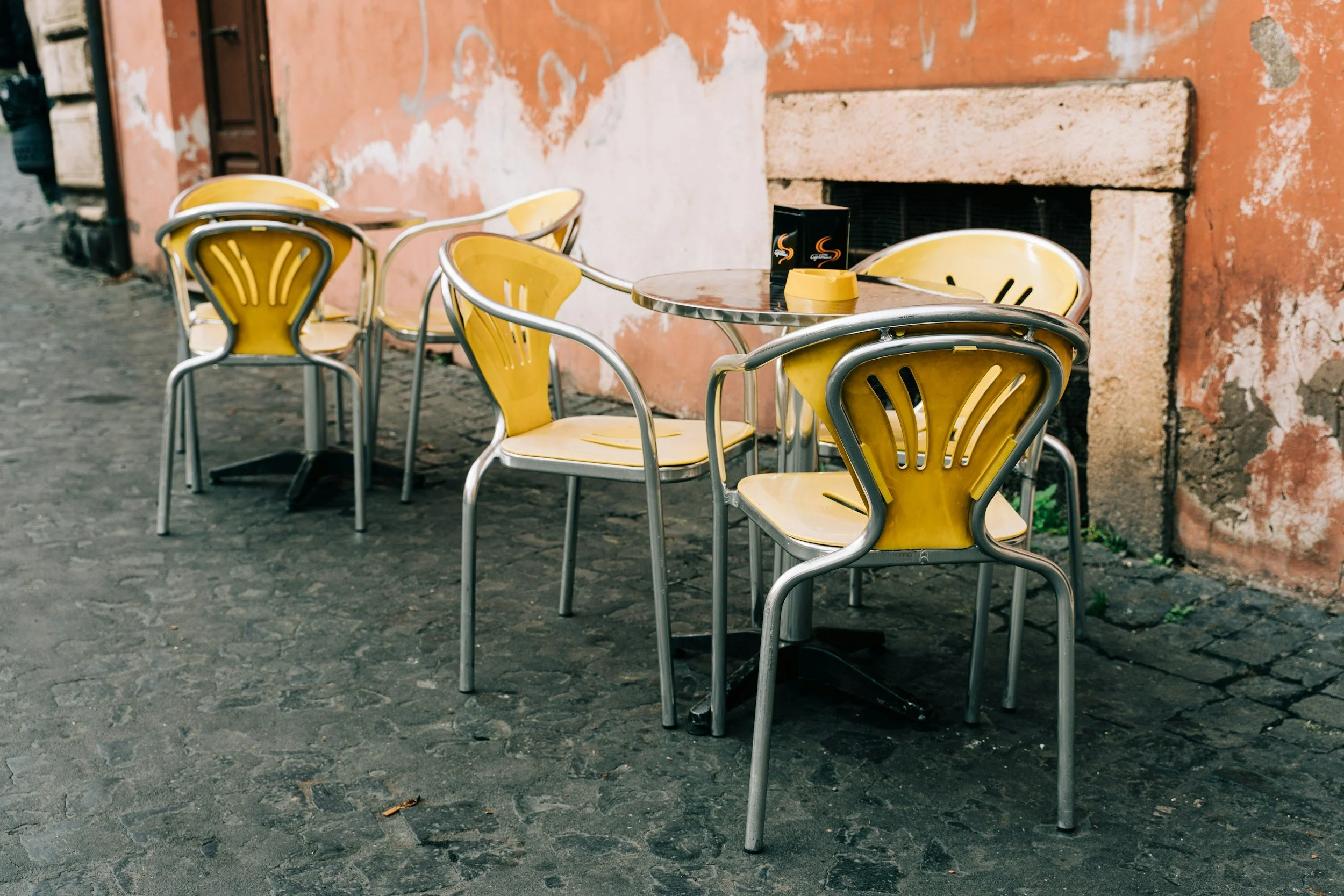 Cafe table and bright yellow chairs outside in front of a wall with aged terracotta colored paint