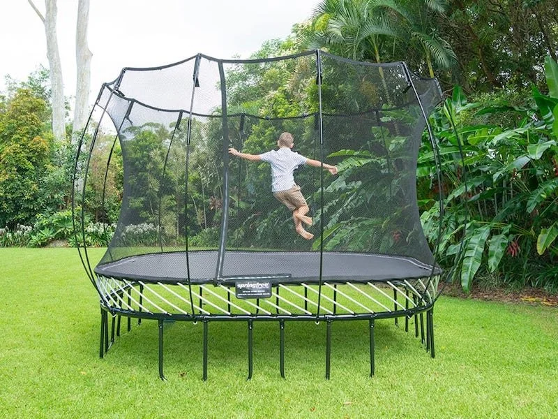 A boy jumping on a Springfree Trampoline in a backyard with lots of greenery.