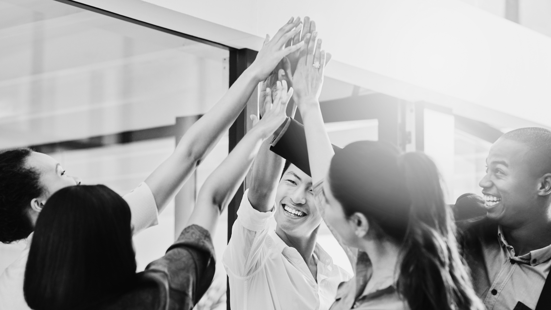 Group of diverse young adults celebrating and giving high-fives inside a building, smiling and happy.