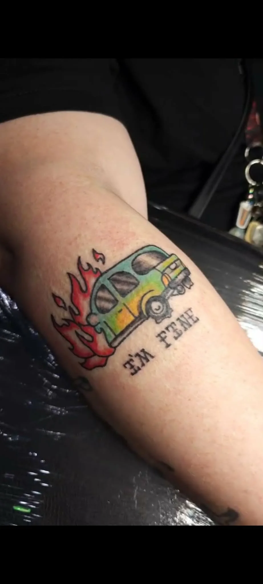 Tattoo of a vintage van with flames behind it, with the words I'm fine" underneath in traditional style.