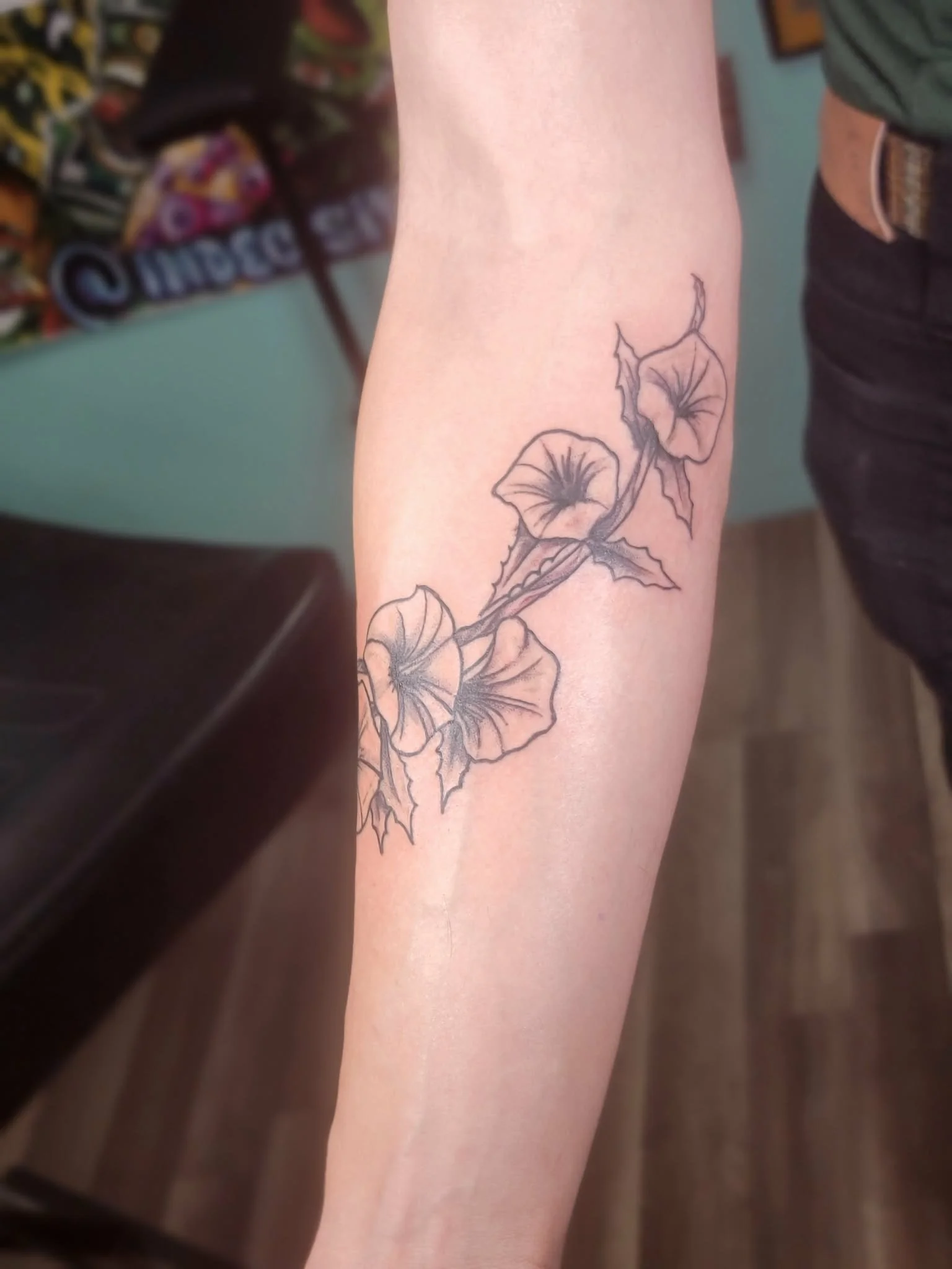 A black ink tattoo of morning glory flowers on a person's forearm.