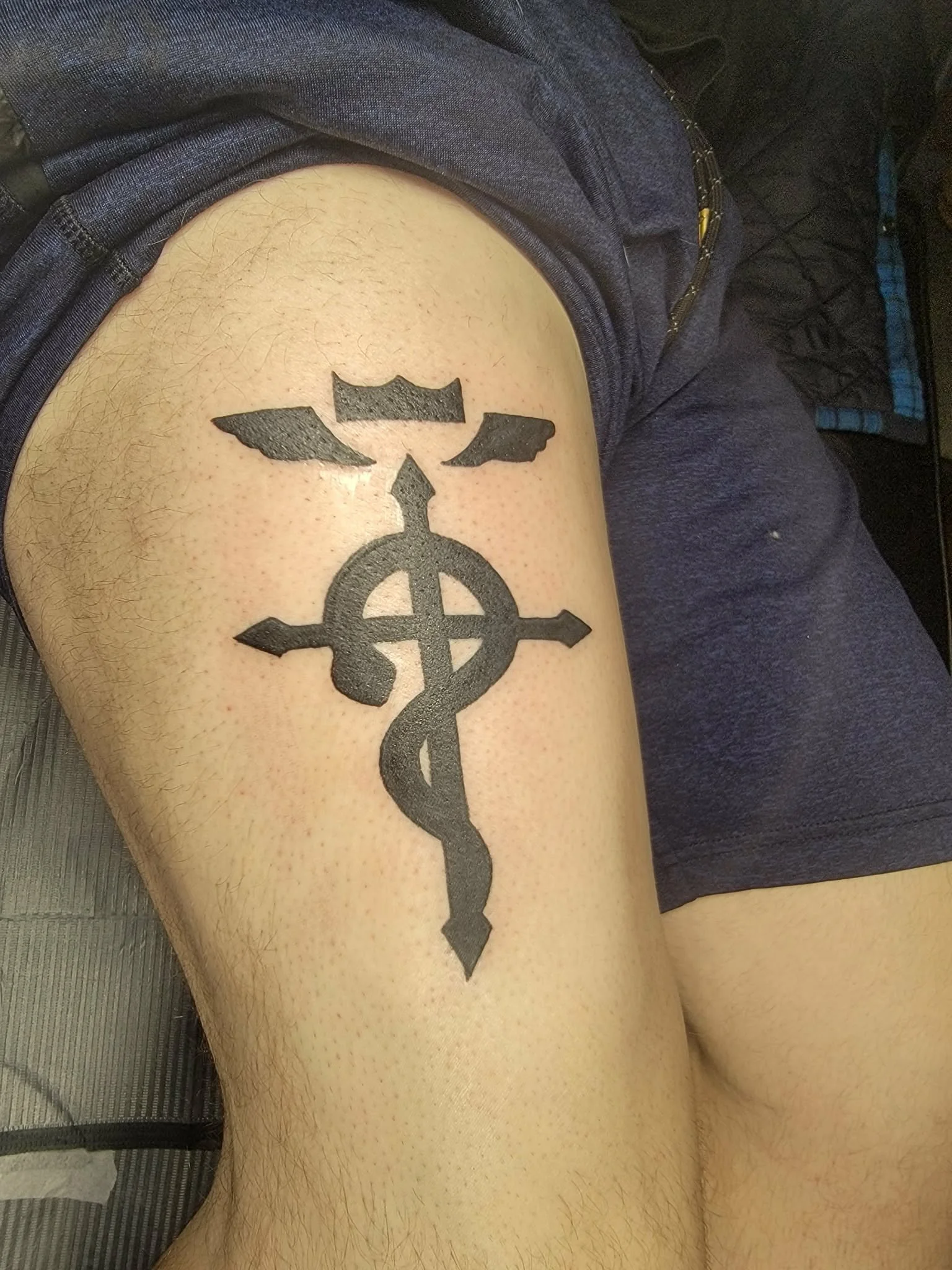 Tattoo of a cross intertwined with a snake on a person's thigh.