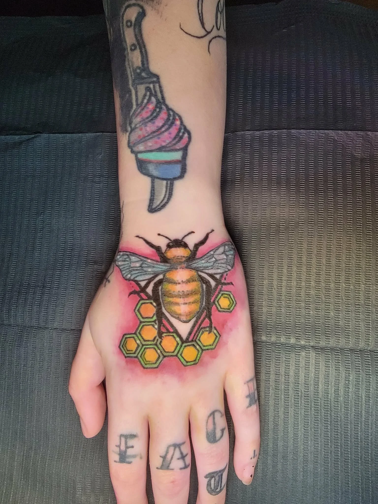 Tattoo of a bee with honeycomb pattern on the hand, and a colorful ice cream cone on the forearm.