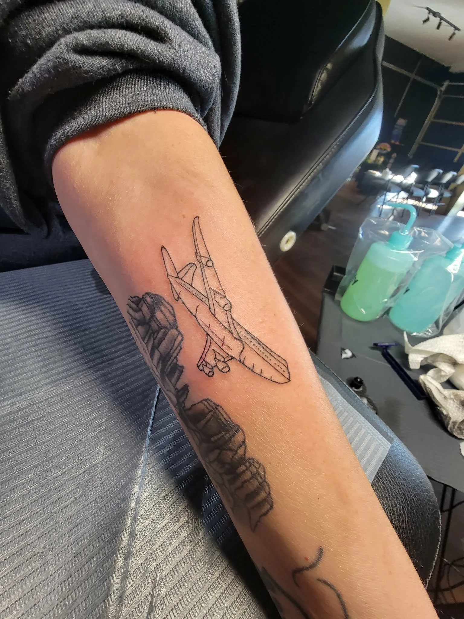 Tattoo of a flying airplane on a person's forearm.
