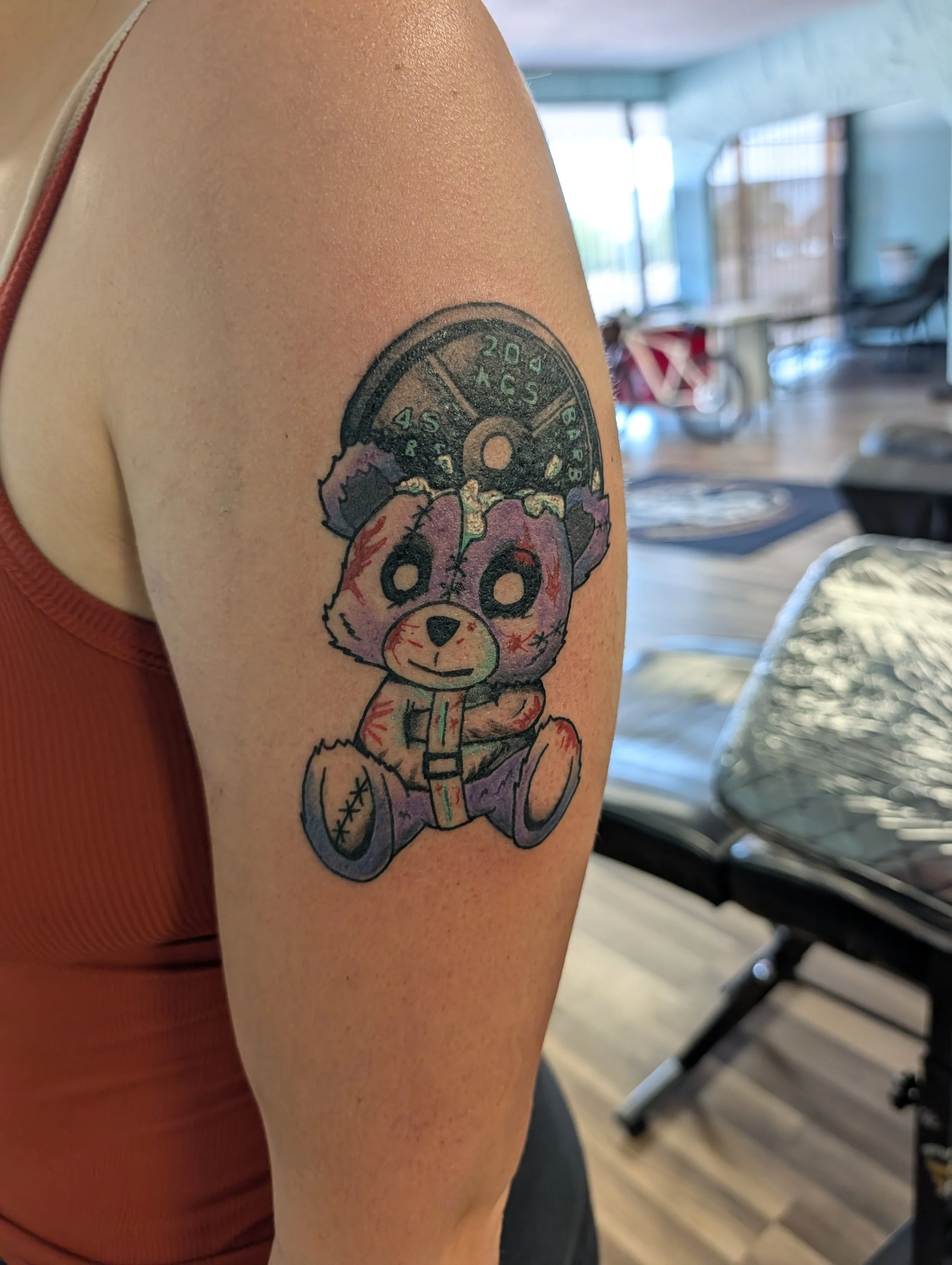 Tattoo of a cute bear holding a popsicle on a person's upper arm with a cartoon-style design.