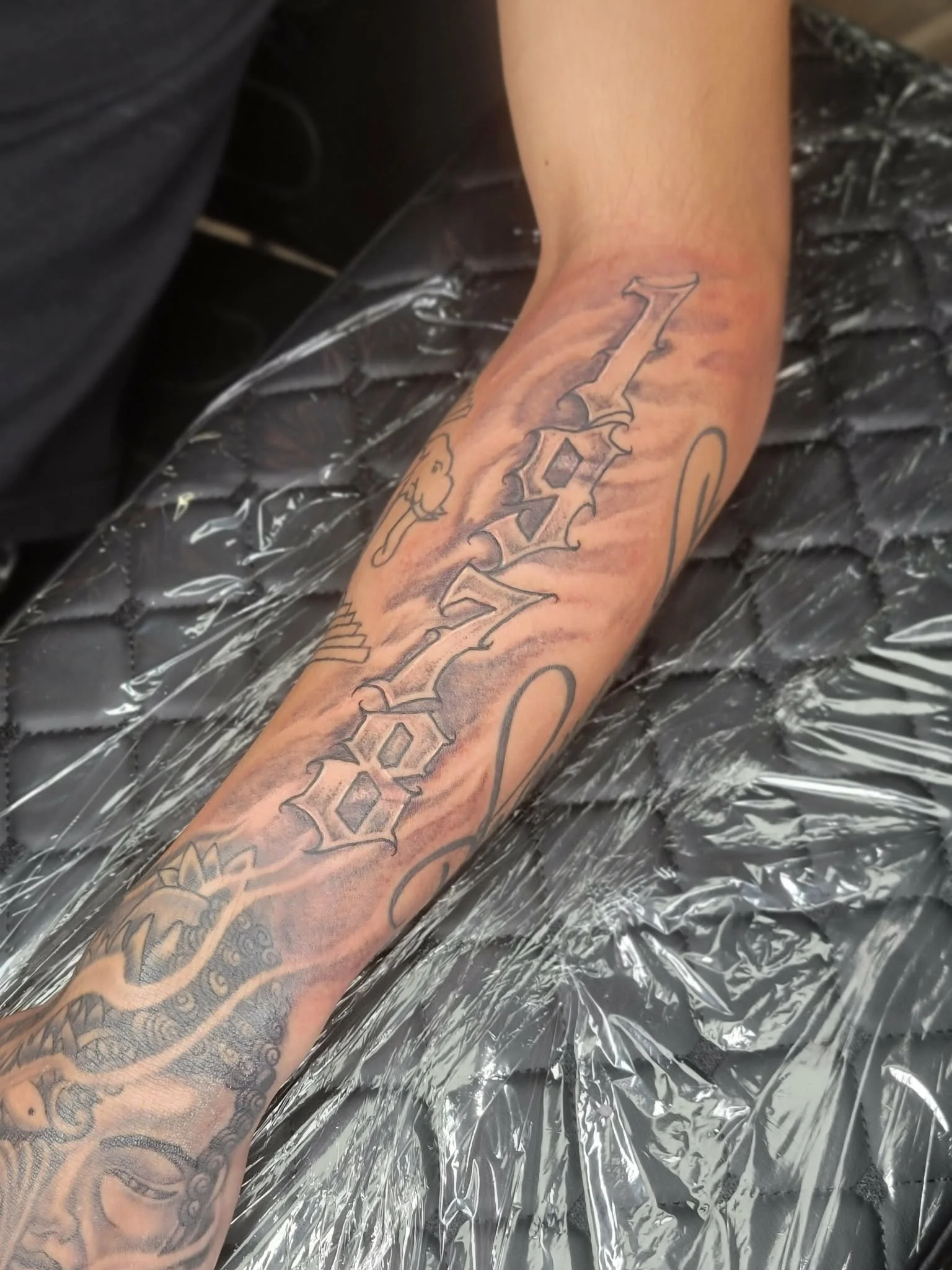 Tattoo on person's forearm with 1978 done in gothic style lettering, surrounded by various black ink designs.