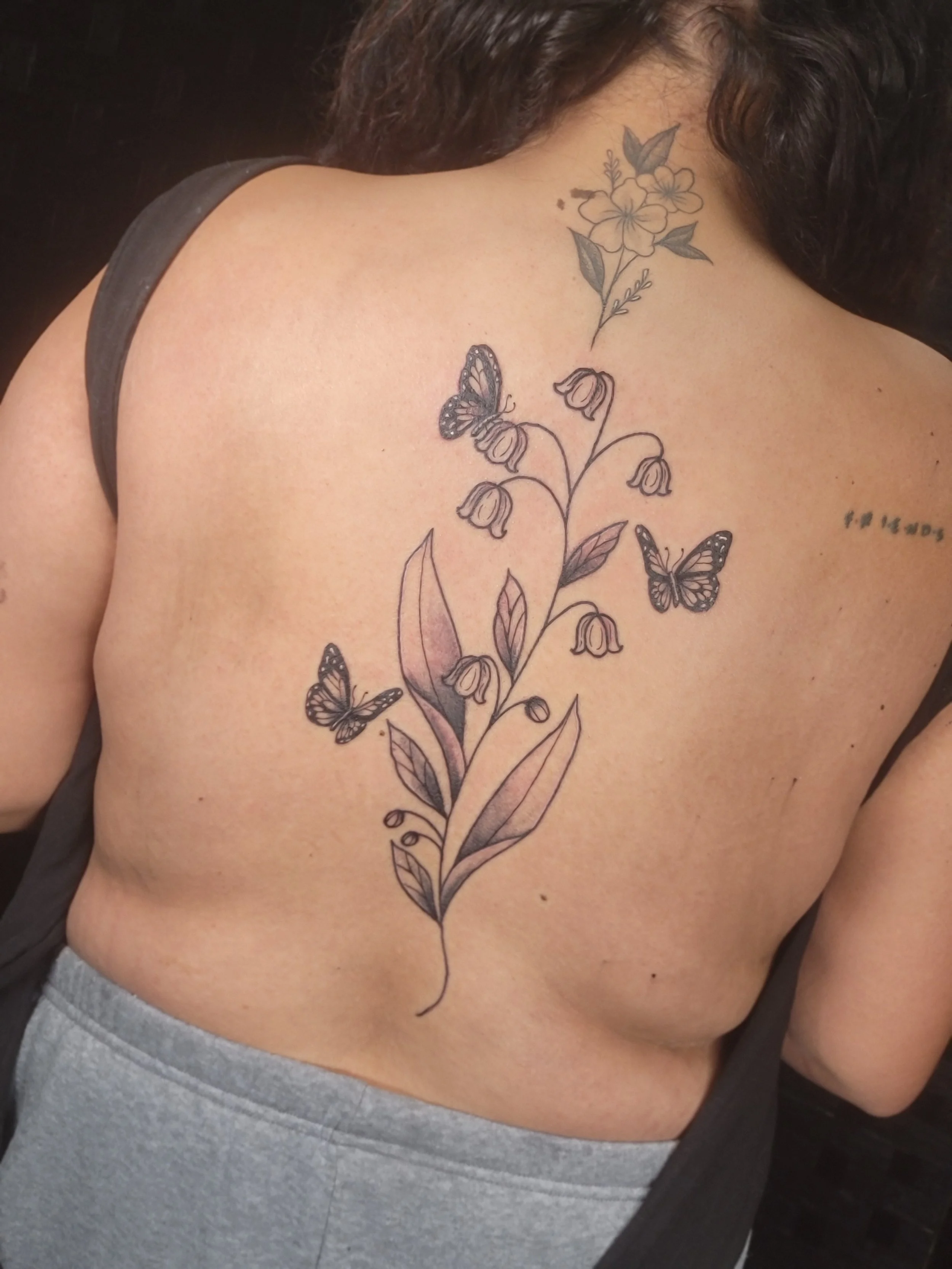 A person's upper back with a floral tattoo featuring flowers and butterflies.