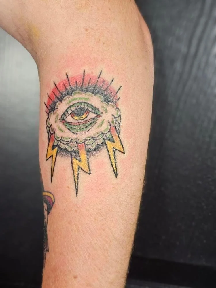 Tattoo of an eye with lightning bolts and a cloud on a person's arm in traditional style.