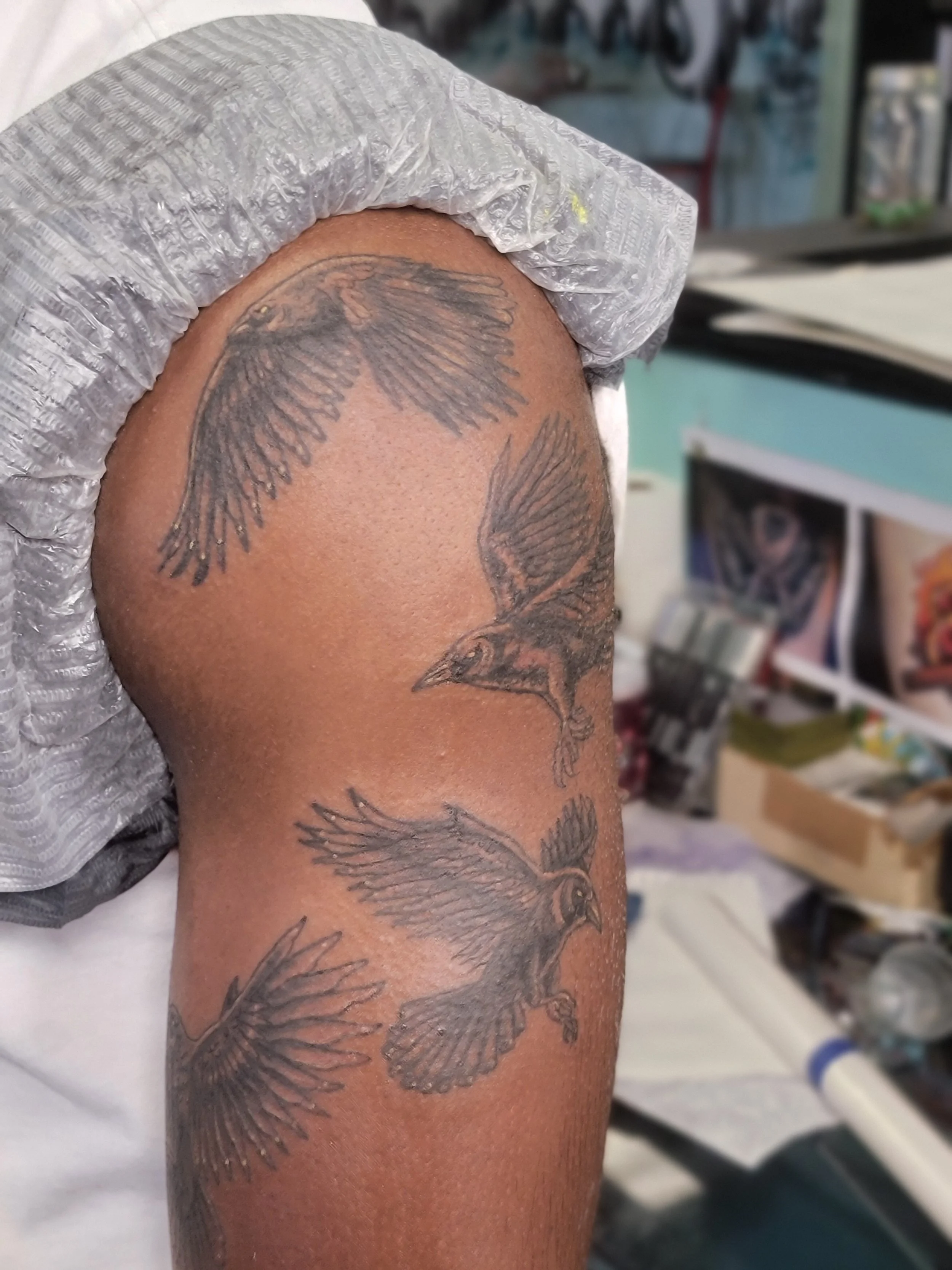 A close-up view of a person's upper arm with multiple tattoos of birds in flight on the skin.