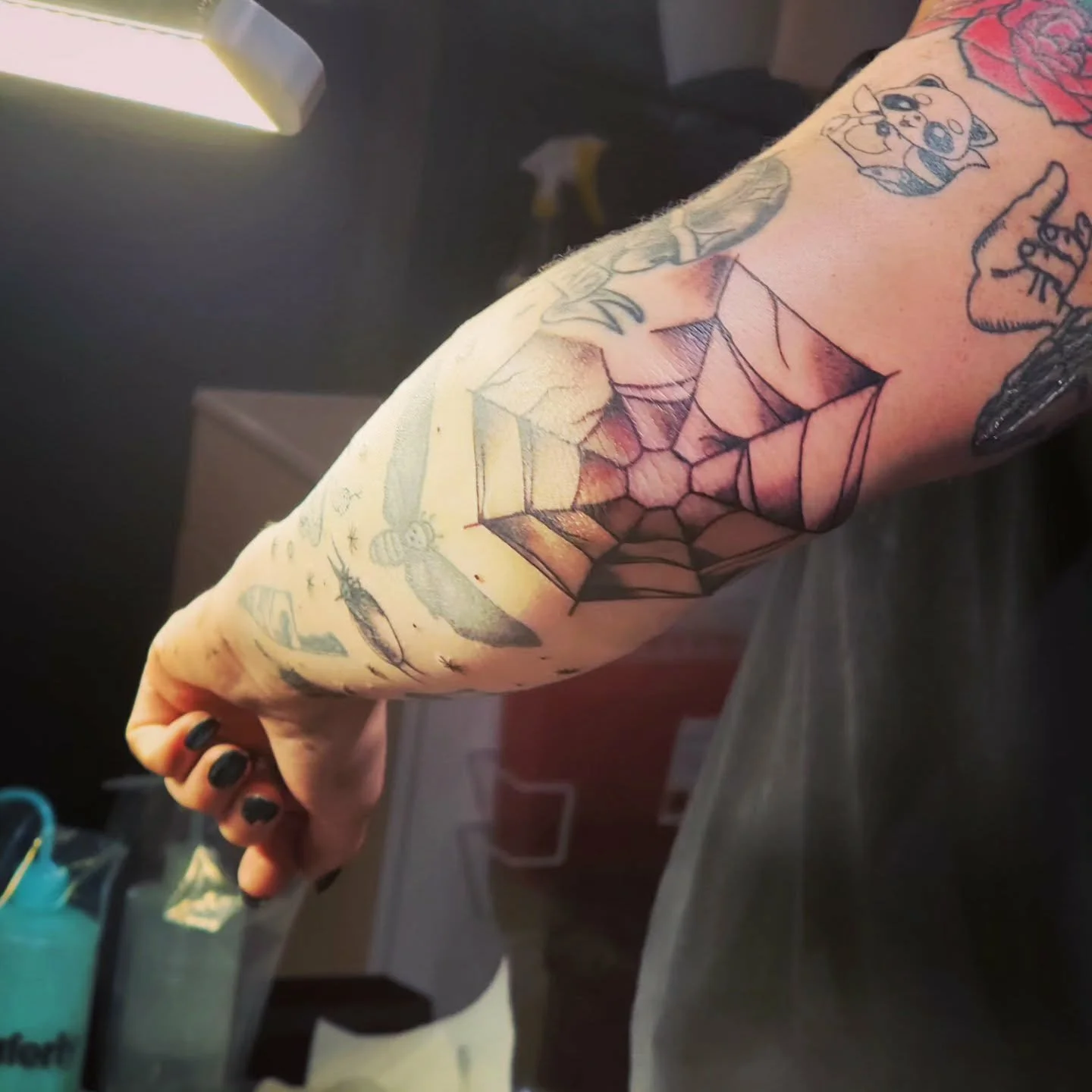 Tattooed arm with a spider web design on the elbow and multiple other tattoos.