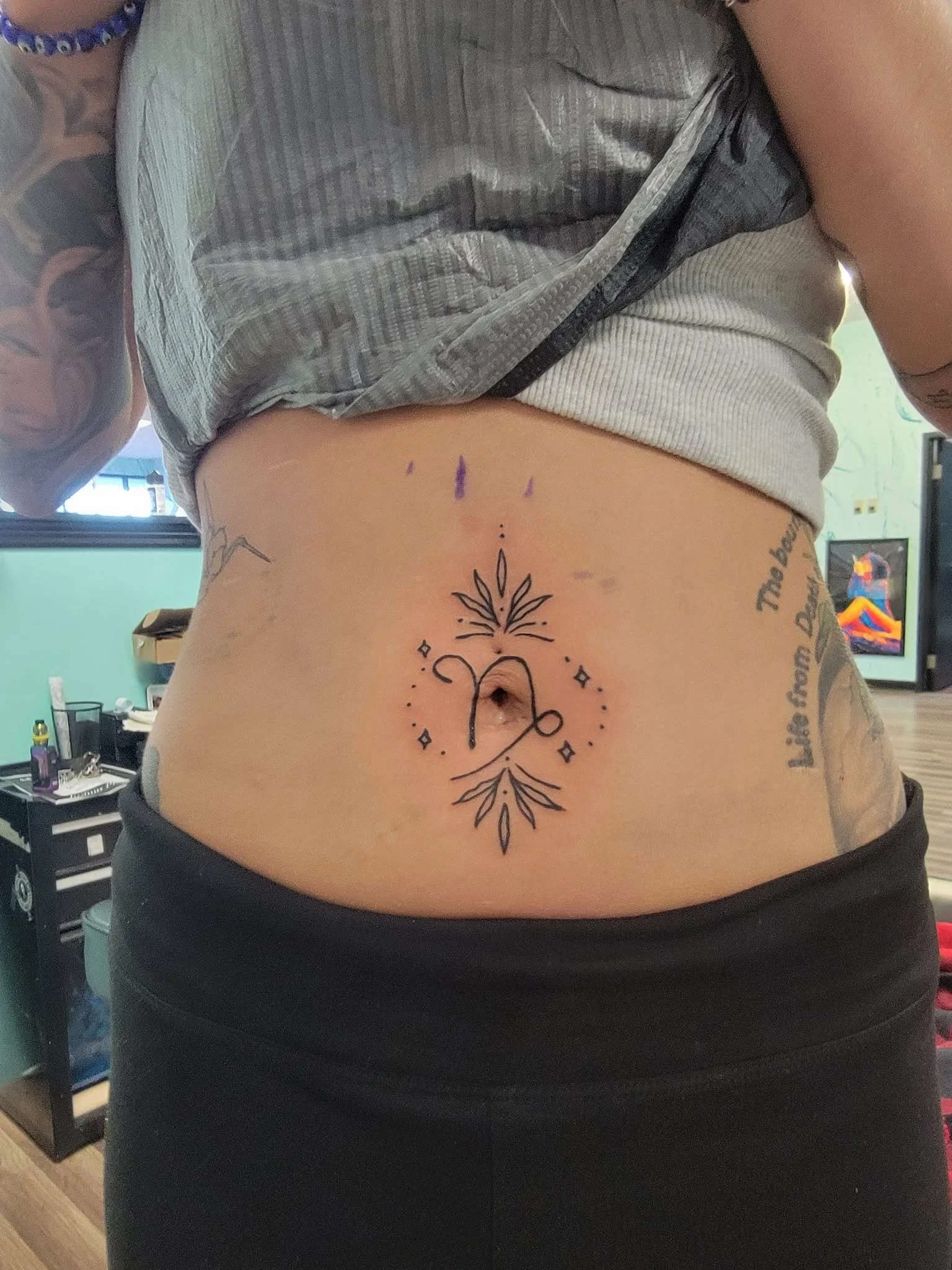 Tattoo of a zodiac sign with decorative lines and diamond shapes on a person's lower abdomen.