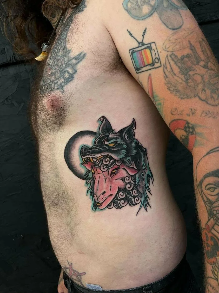 Tattoo of a wolf and a ram's head on a person's side in traditional style.