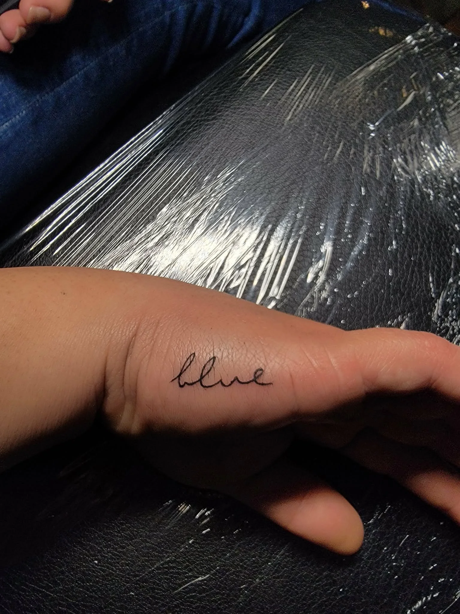 A hand with a small tattoo of the word 'blue' written in cursive on the middle finger.