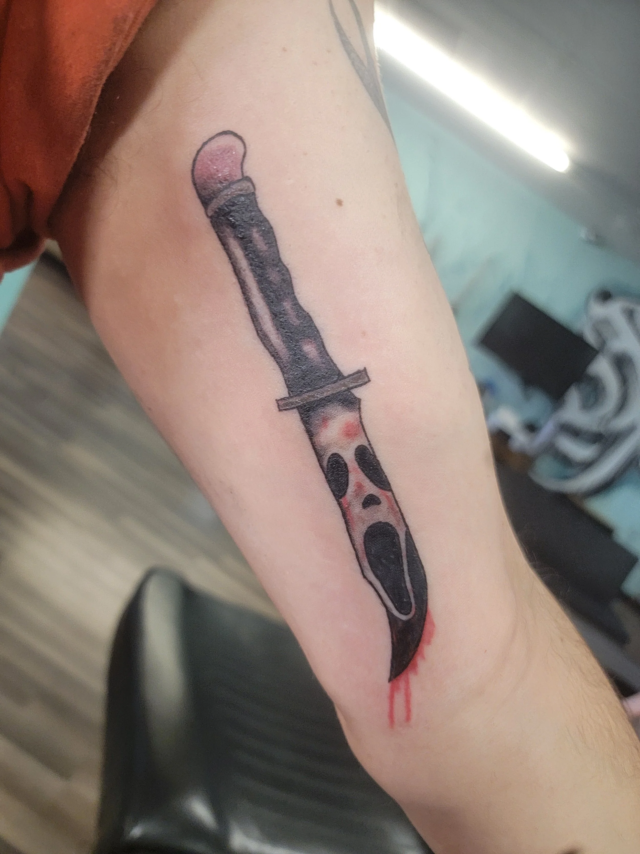 Tattoo of an open knife with blood on the blade, located on a person's arm.