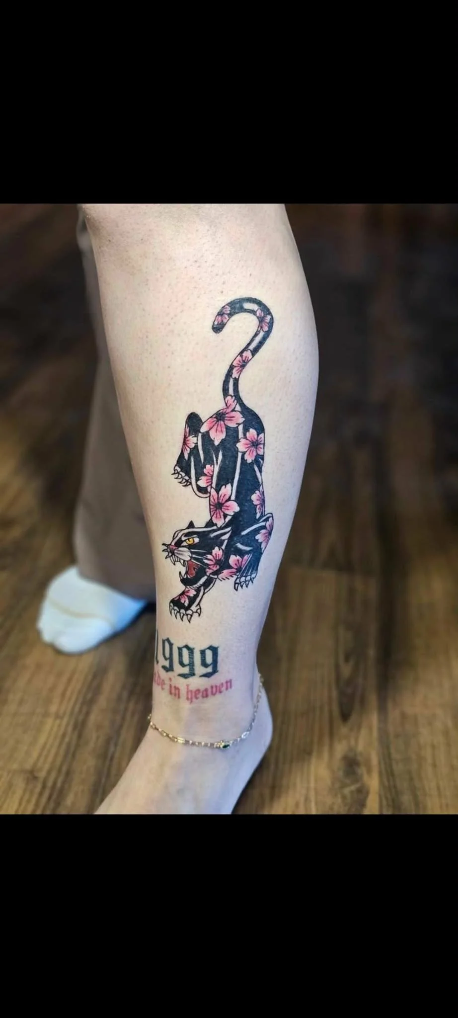 Tattoo of a black panther with pink flowers, the year 1999 on a person's leg.