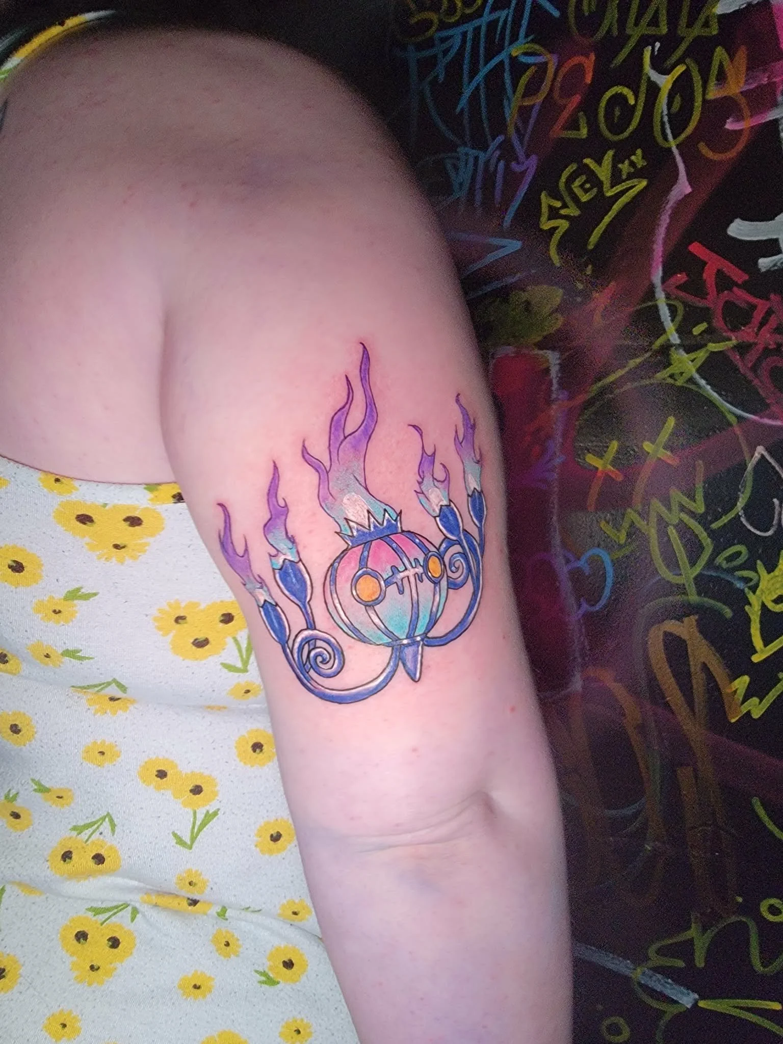 Tattoo of a stylized, colorful celestial body with flames and abstract design on a person's upper arm.