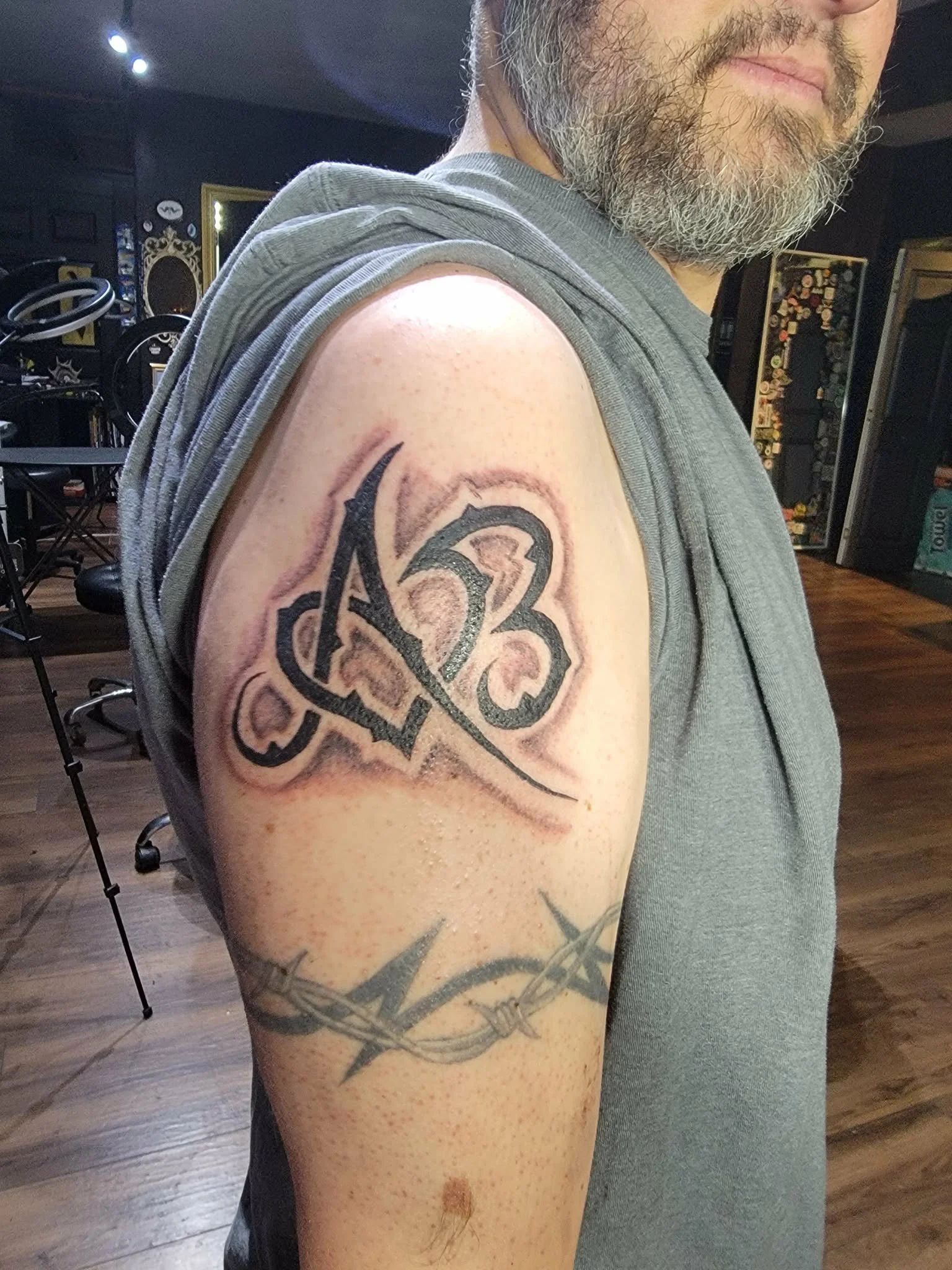 Tattoo of the initials 'AB' with a stylized font on upper arm, and a barbed wire design below it on the same arm.