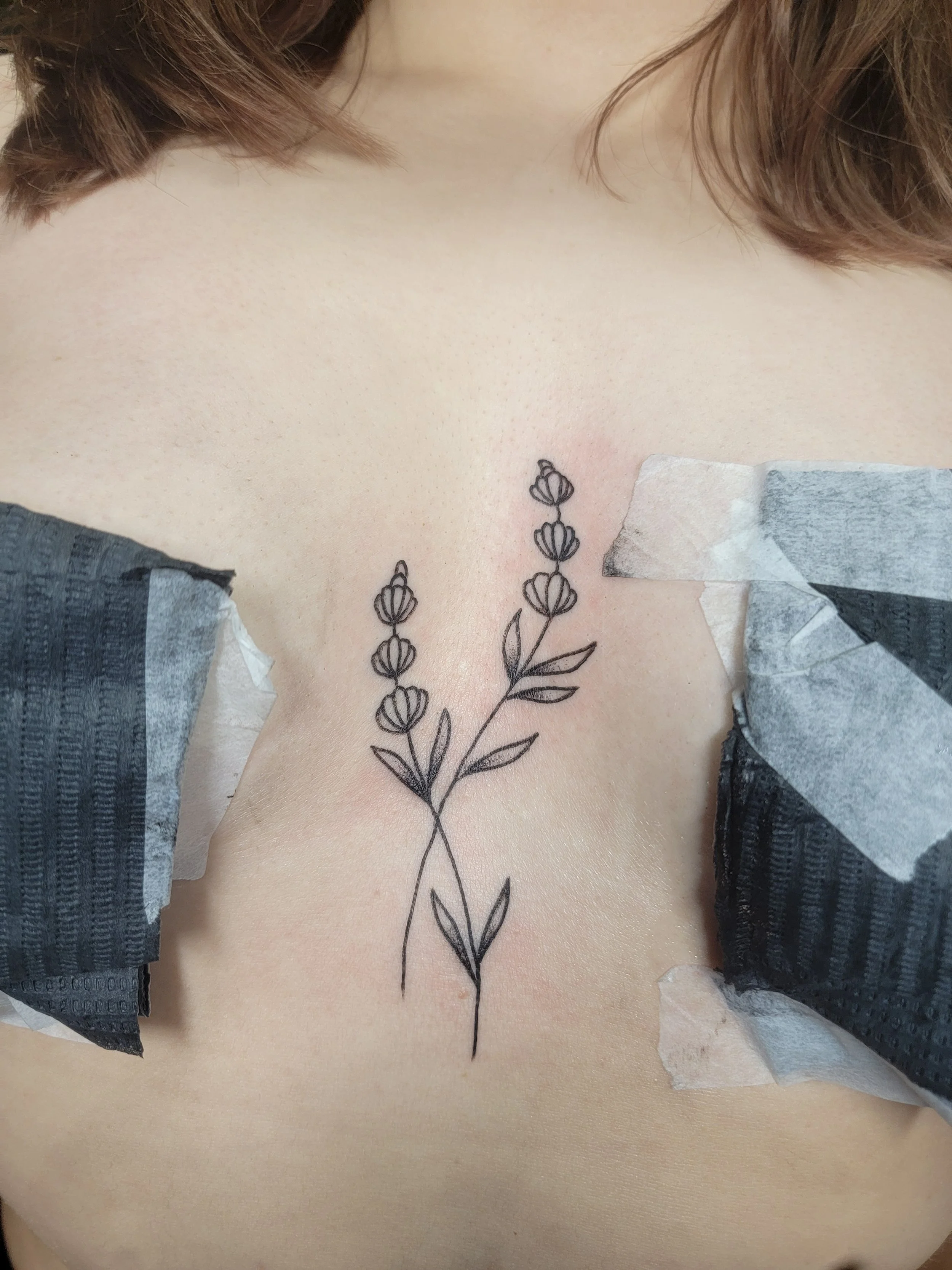 A person's chest with a tattoo of a flowering plant on the skin, with some tape and tissue paper nearby.