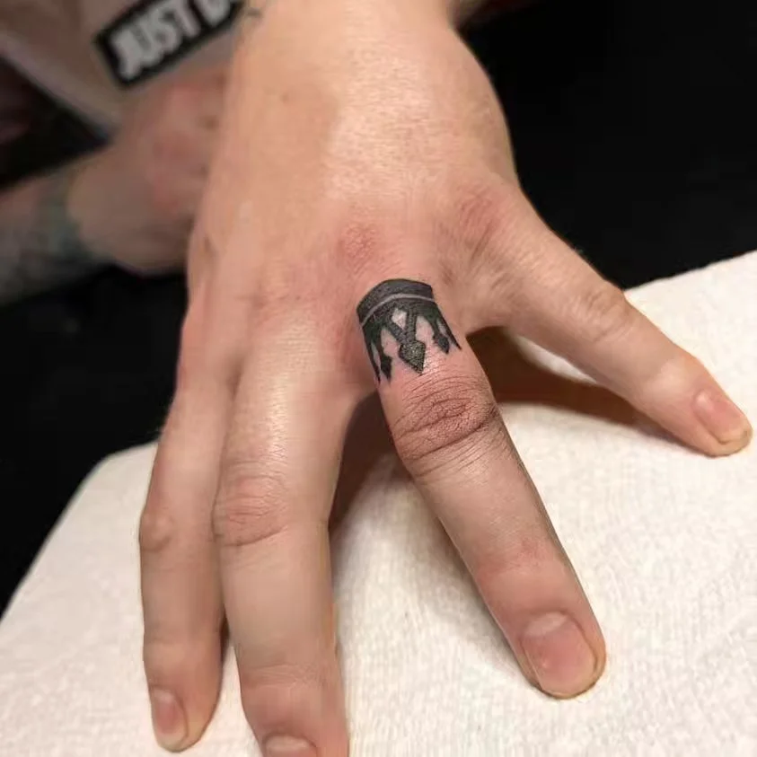 A person's hand with tattoos on the index finger and surrounding area, resting on a white surface.