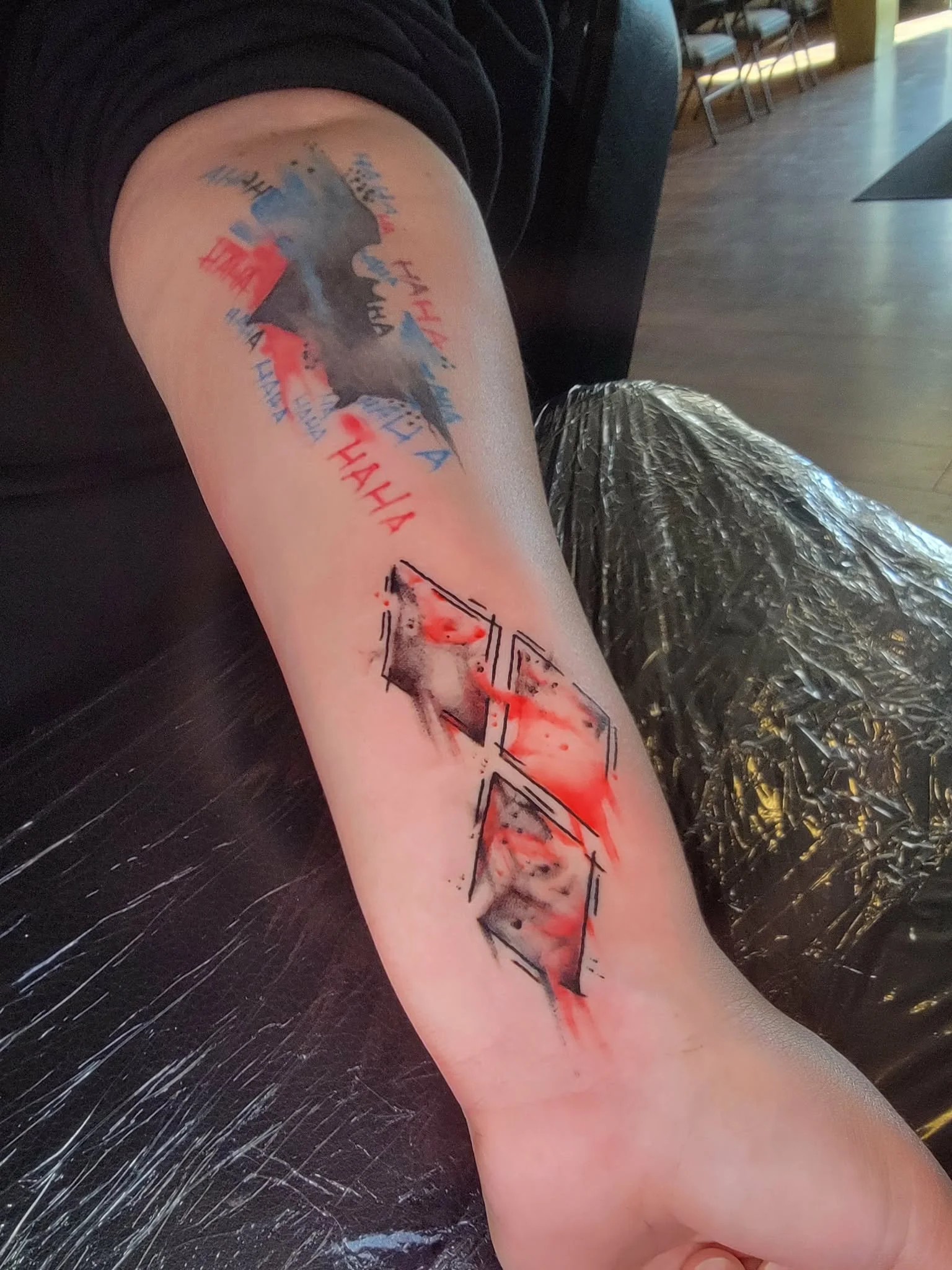 Tattoo on person's arm featuring stylized watercolor diamonds, with a black and red color scheme.