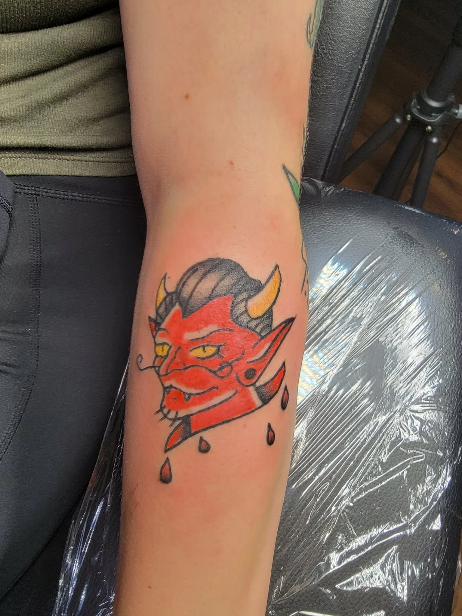 Tattoo of a red devil with black horns, yellow eyes, and black teardrops on the arm in traditional style.
