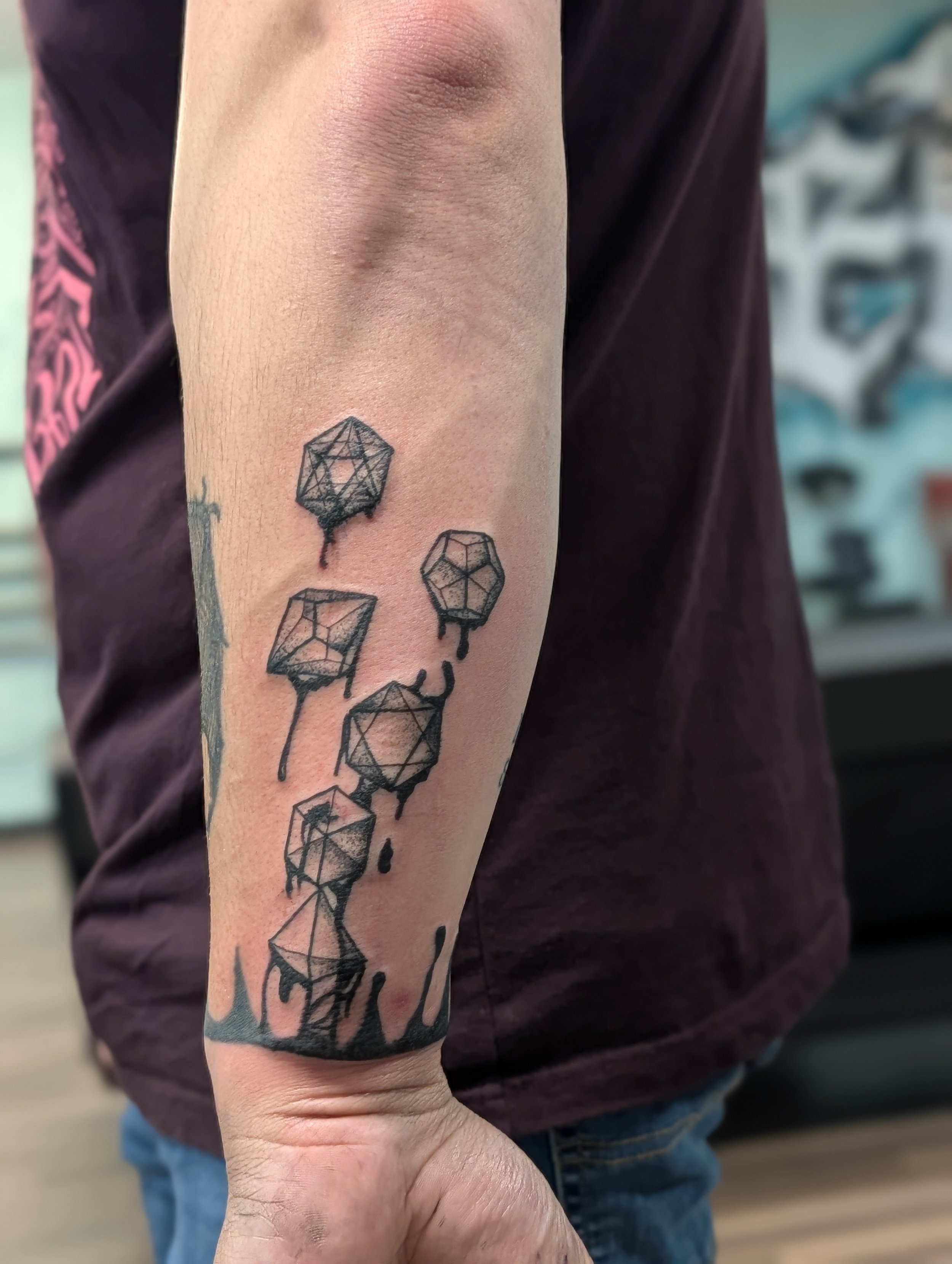 A person's arm with a tattoo of geometric shapes resembling dice, with some shapes dripping ink.