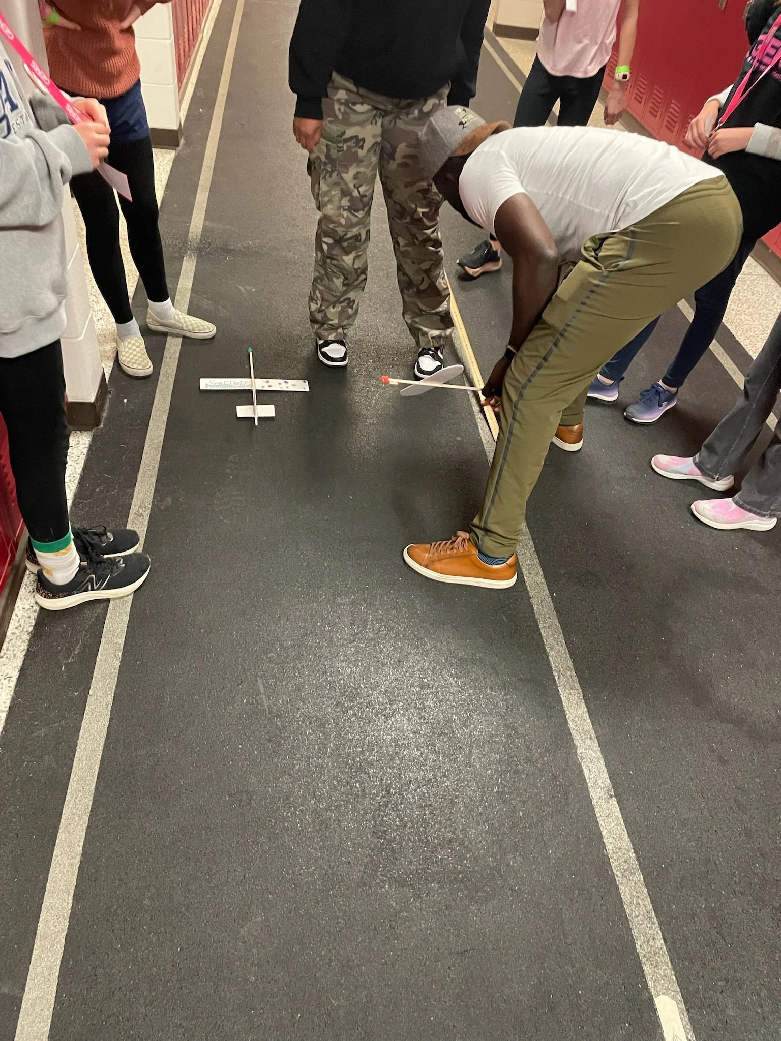 Students gathered in a school hallway, observing a science experiment involving a small rocket and launch pad.