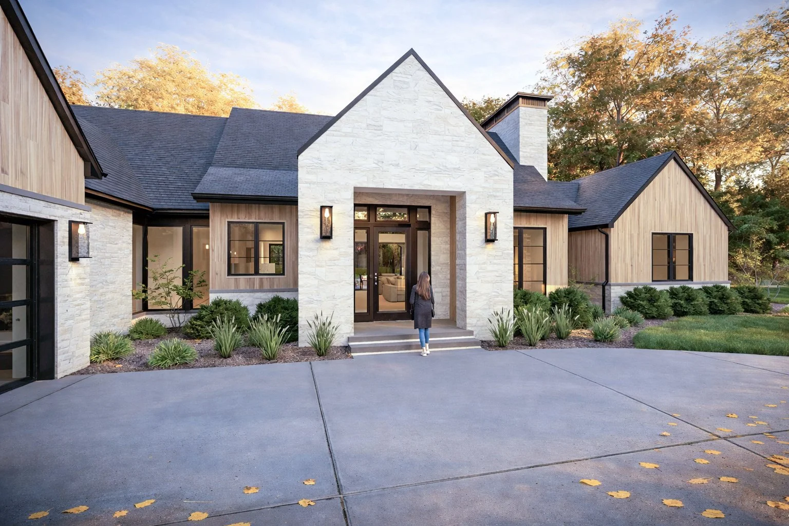 Concrete driveway leading up to a luxury home with an attached multi-car garage featuring black glass panel doors.