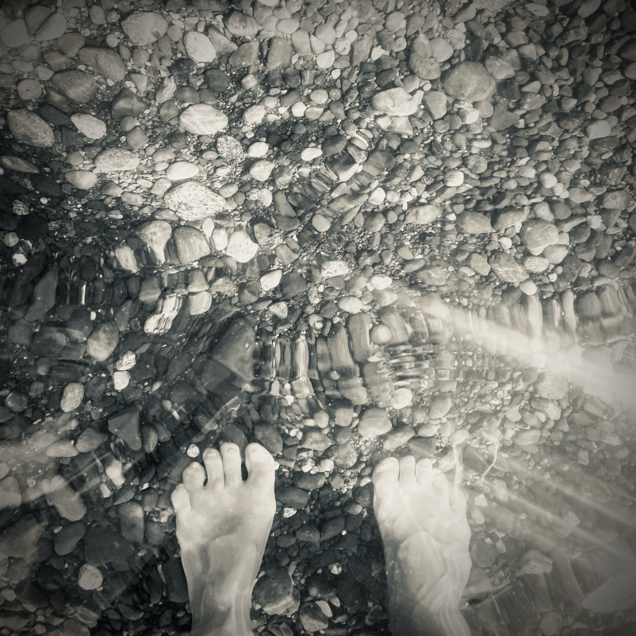 Captain e2 Brewster's feet on a rocky shoreline along the Salish Sea, among pebbles, gravel, and scattered larger stones.