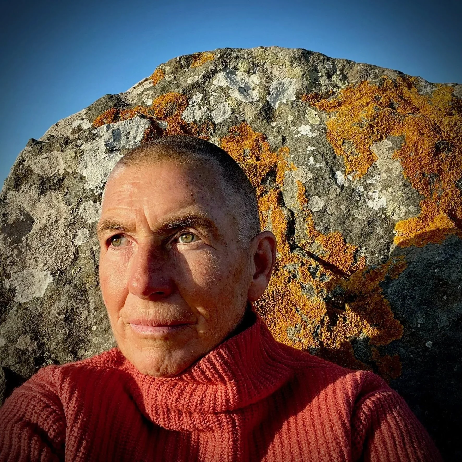 Captain e2 Brewster in front of a colorful lichen-covered rock, wearing a coral colored sweater.