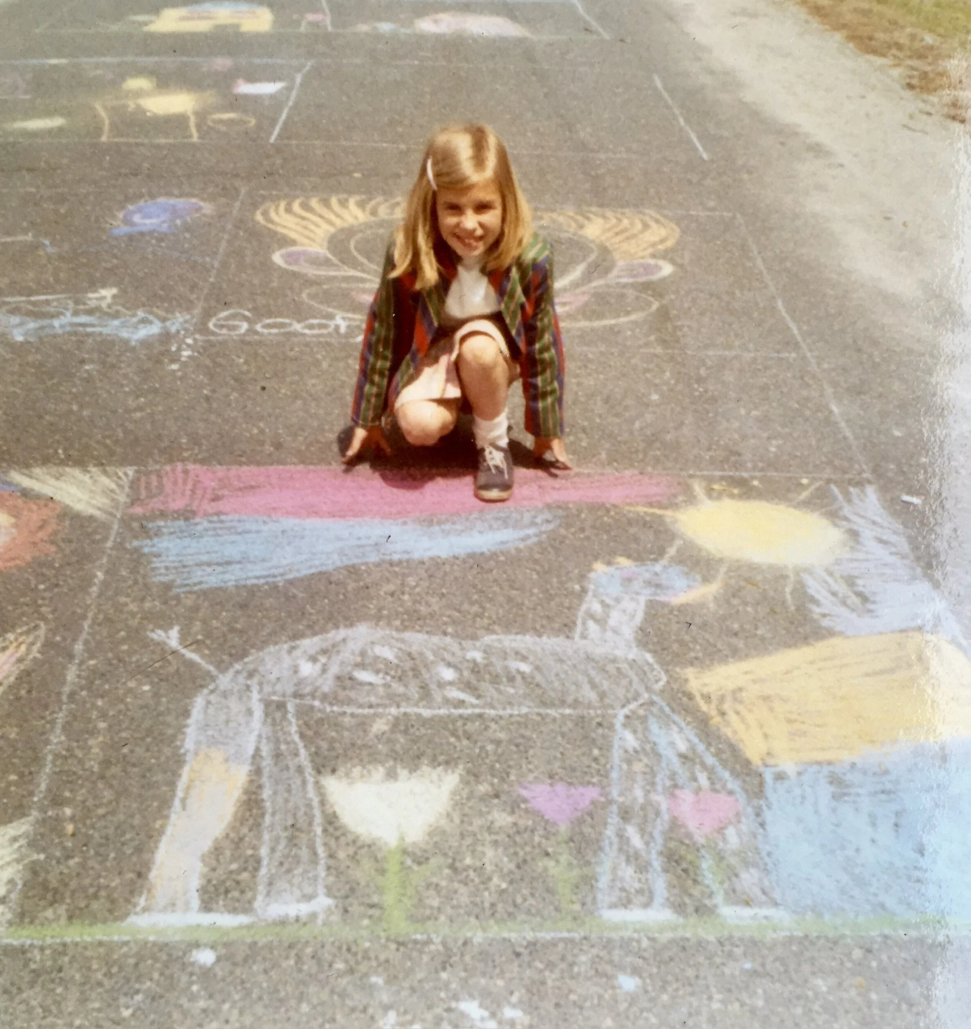 e2 Brewster as a child, kneeling on a colorful chalk-decorated cement play court, smiling.