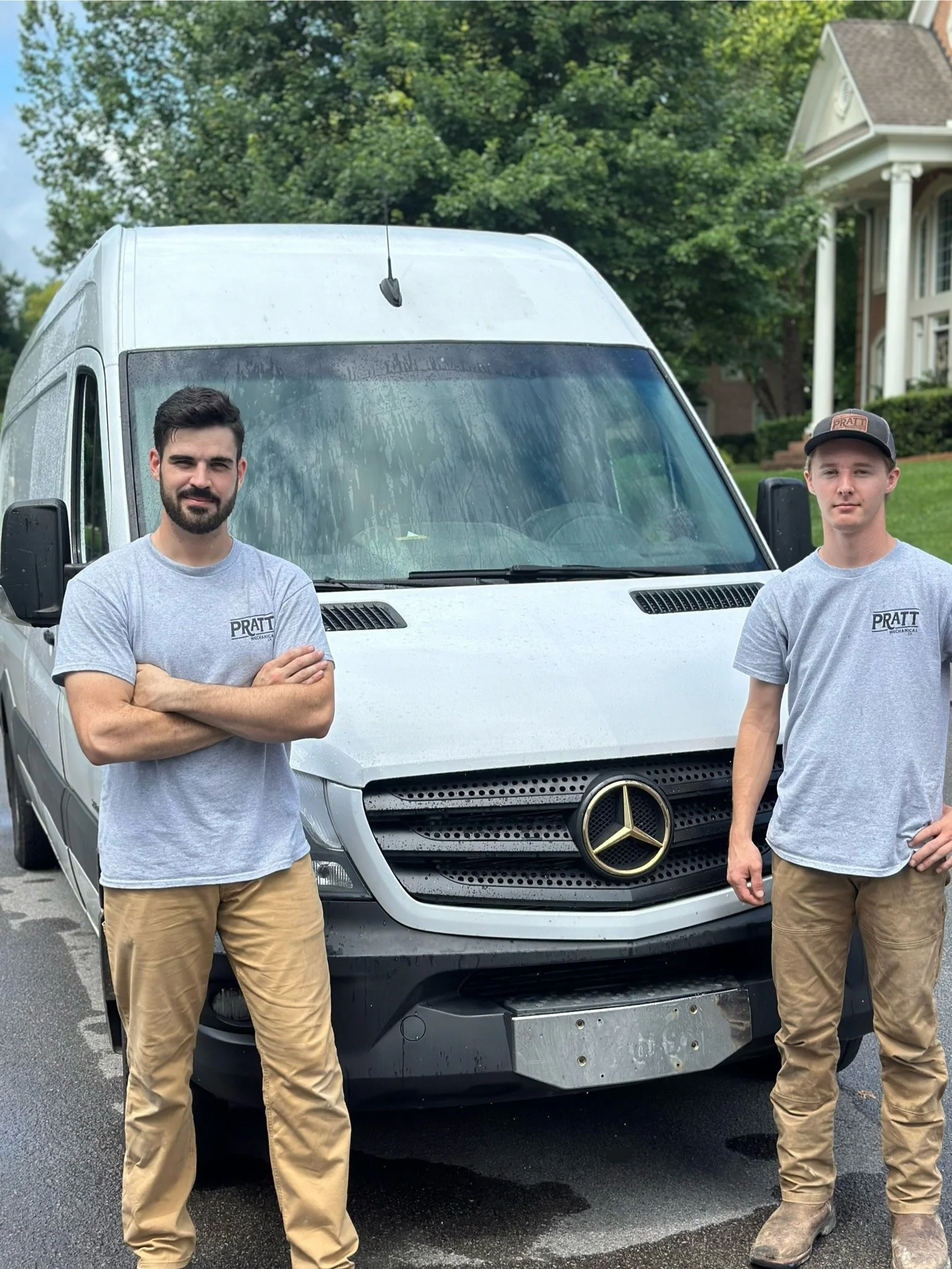 Two men standing in front of a white Mercedes-Benz van, wearing gray Pratt shirts and khaki pants, outdoors on a residential street.