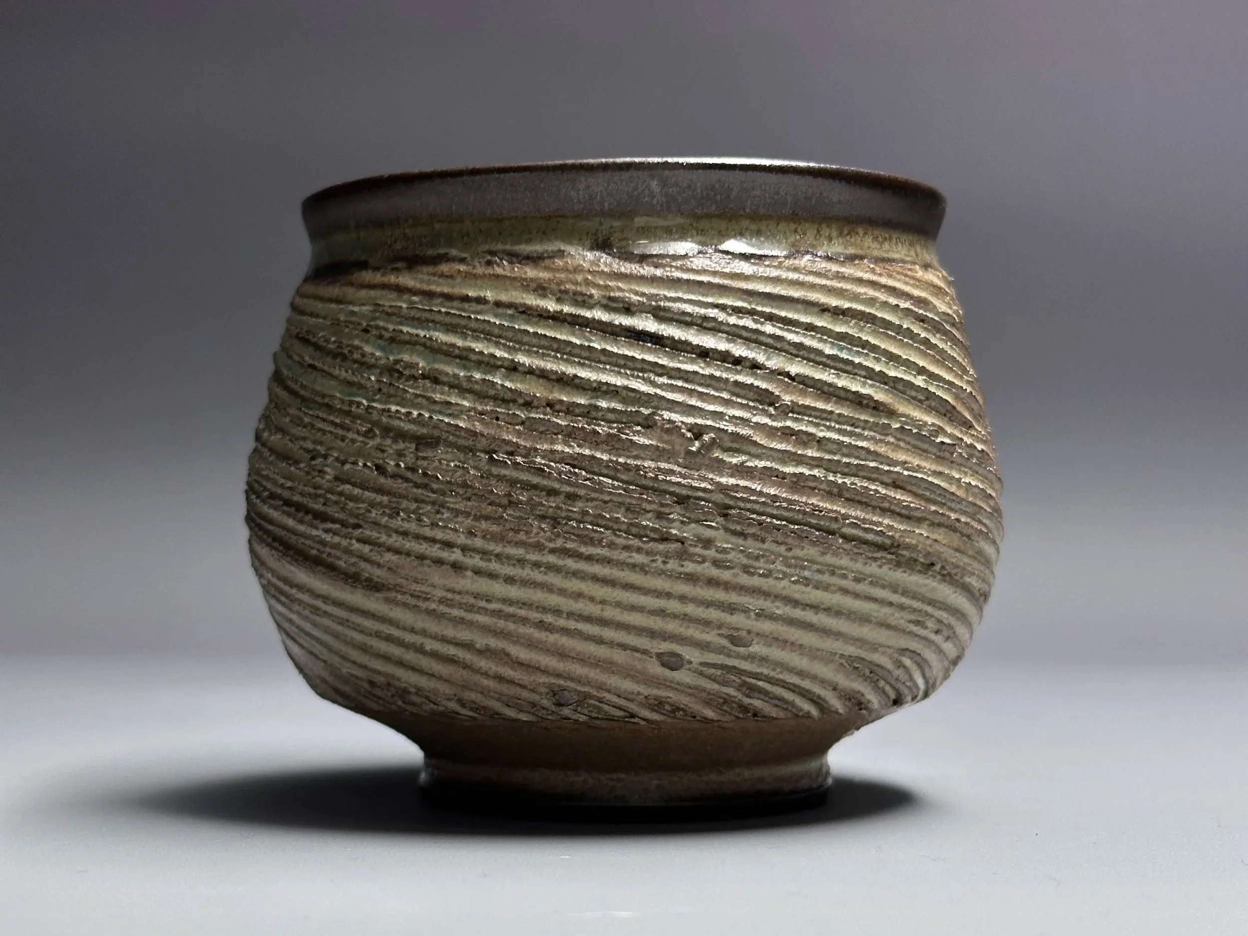 Close-up of a textured ceramic pot with horizontal ridges, against a plain background.