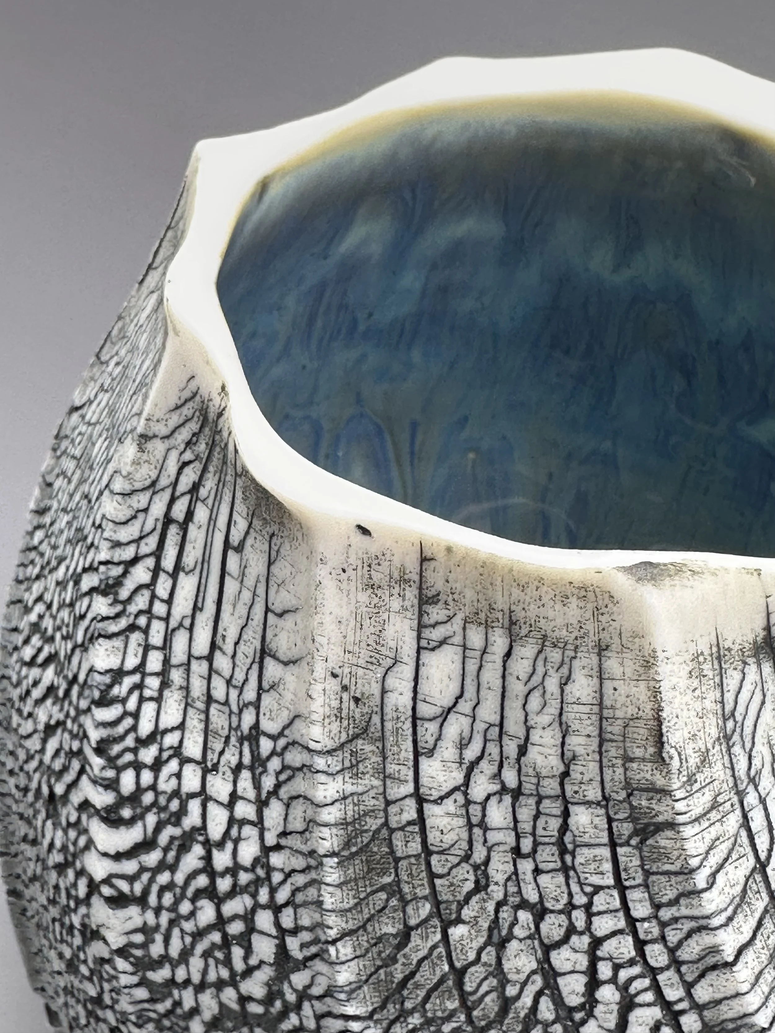 Close-up of a ceramic vase with a textured exterior resembling tree bark and a blue glazed interior.