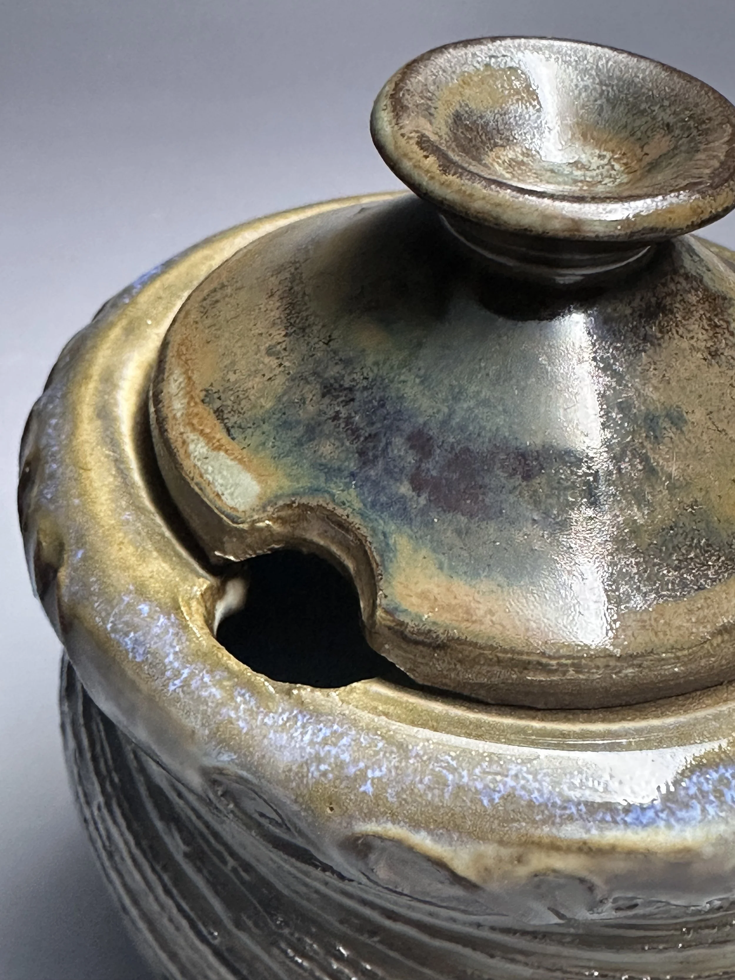 Close-up of a metallic, antique-looking container with a lid, showing signs of tarnish and aging.