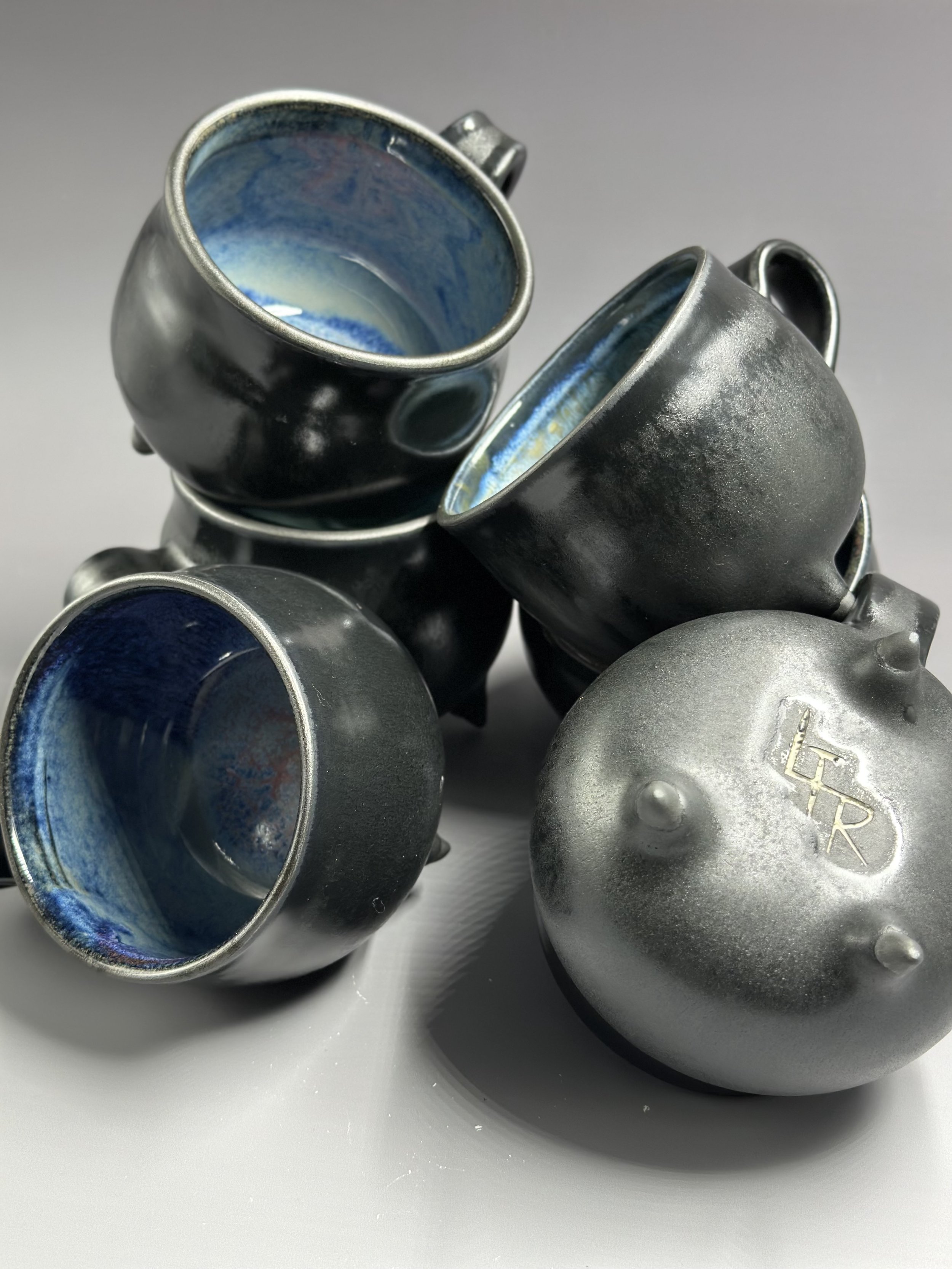 Group of small, metallic, rounded mugs with blue and white glazed interiors, arranged on a plain surface.