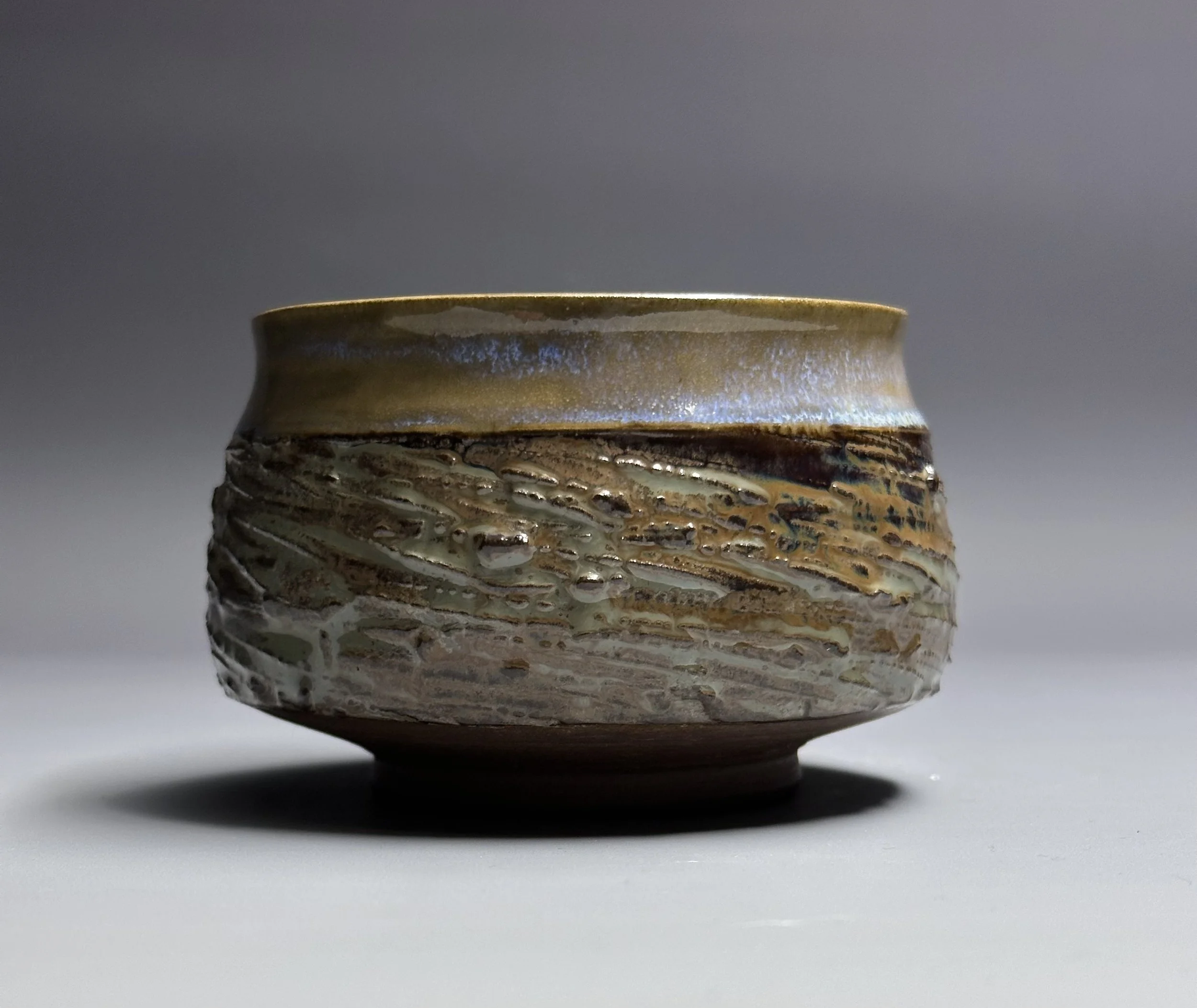 A ceramic bowl with a textured, earthy design, placed on a neutral surface with a plain gray background.