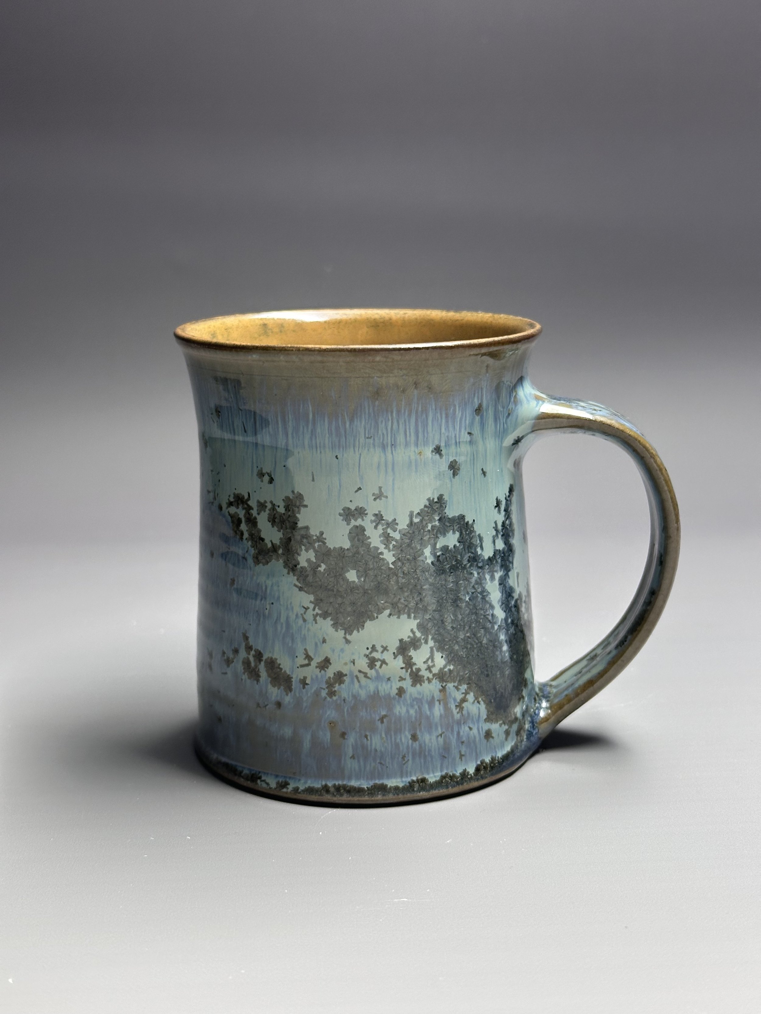 A ceramic mug with a blue and brown glaze, featuring a tree-like pattern on its surface.