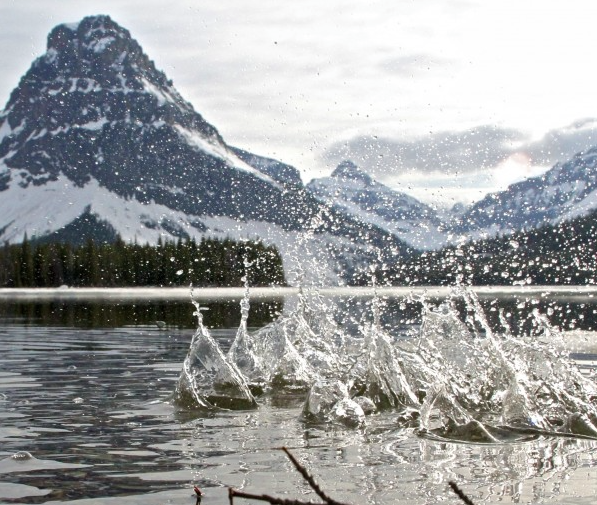 Splashes in a lake with snowy mountains and cloudy sky in the background.