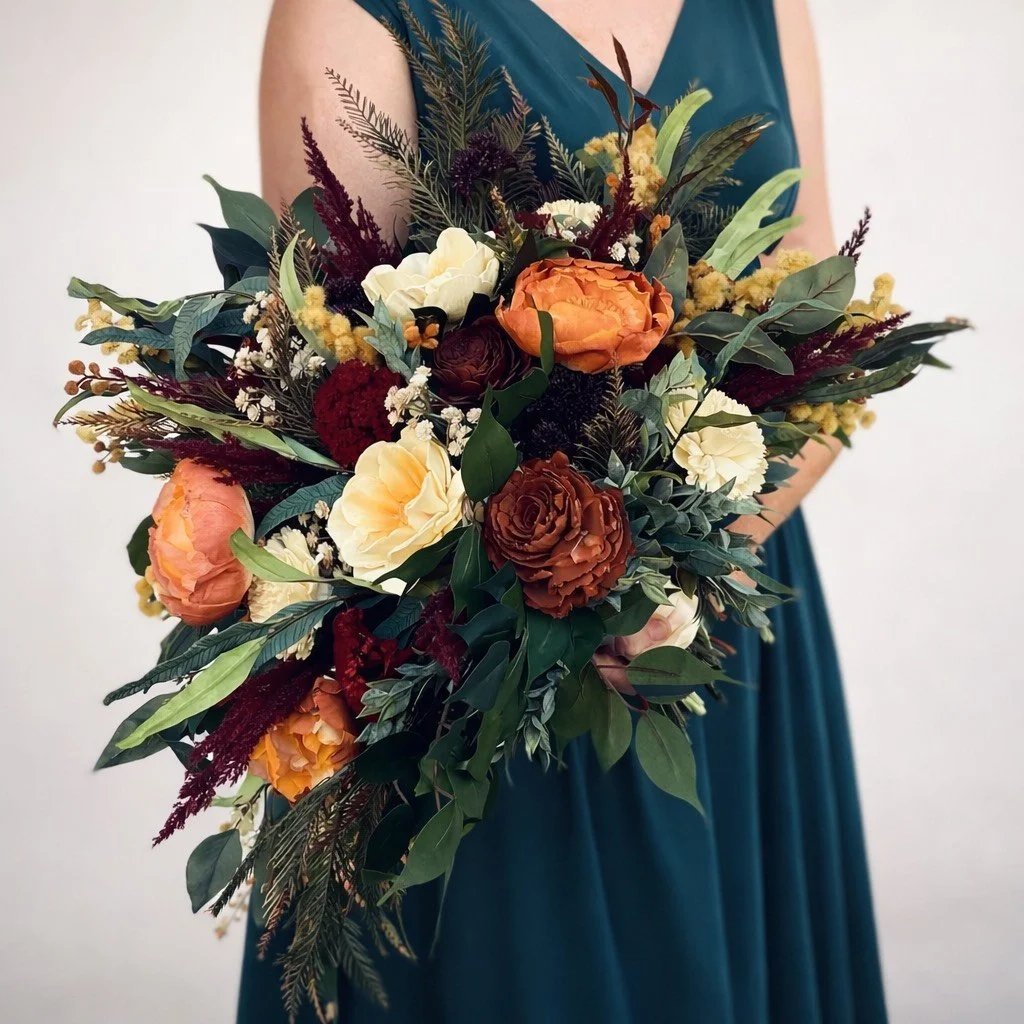 Woman in teal dress holding a large bouquet of mixed flowers, including orange, cream, and dark red blooms, with greenery and foliage.