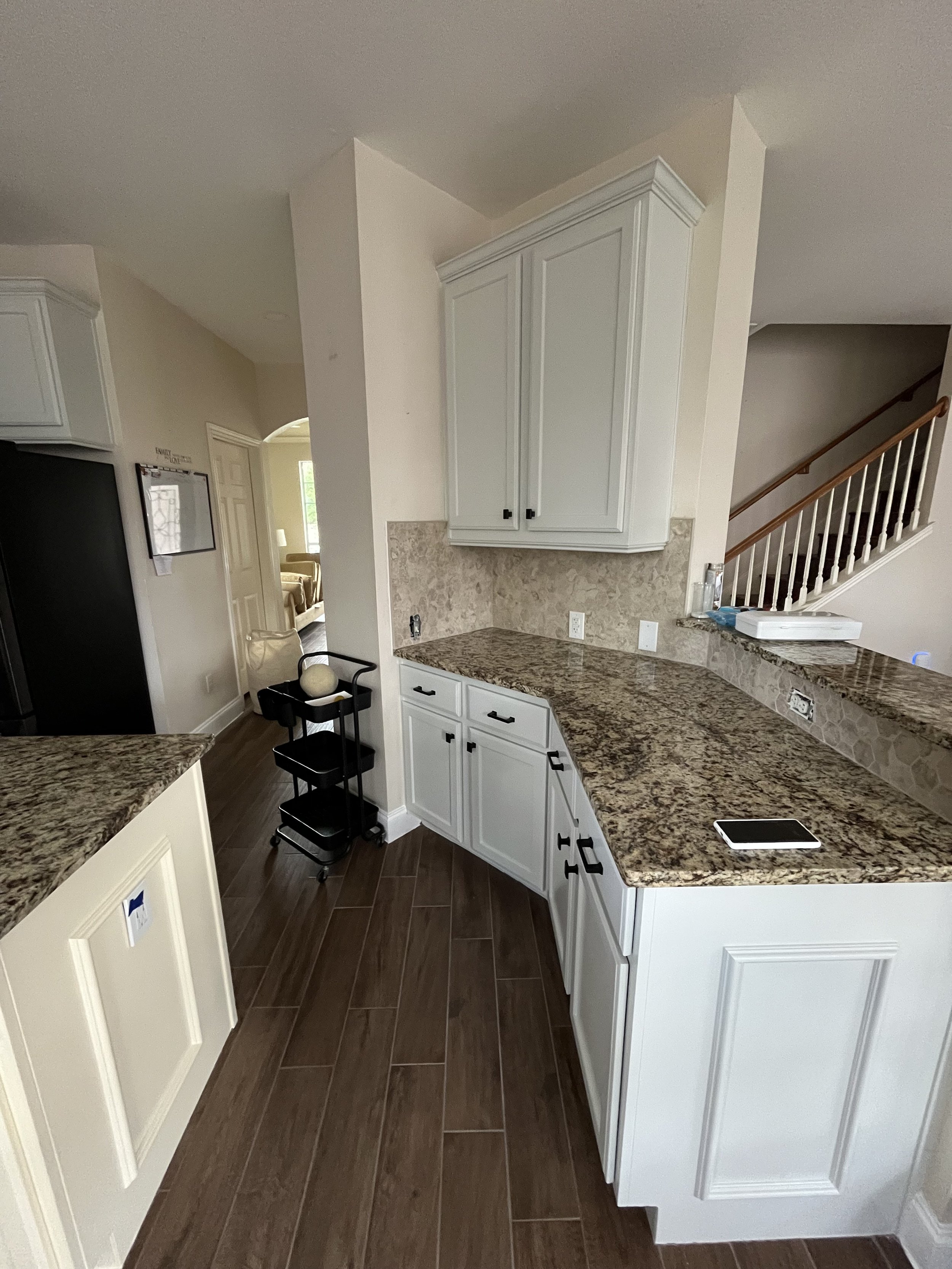 Kitchen with white cabinets, granite countertops, brown tile flooring, and a staircase in the background.