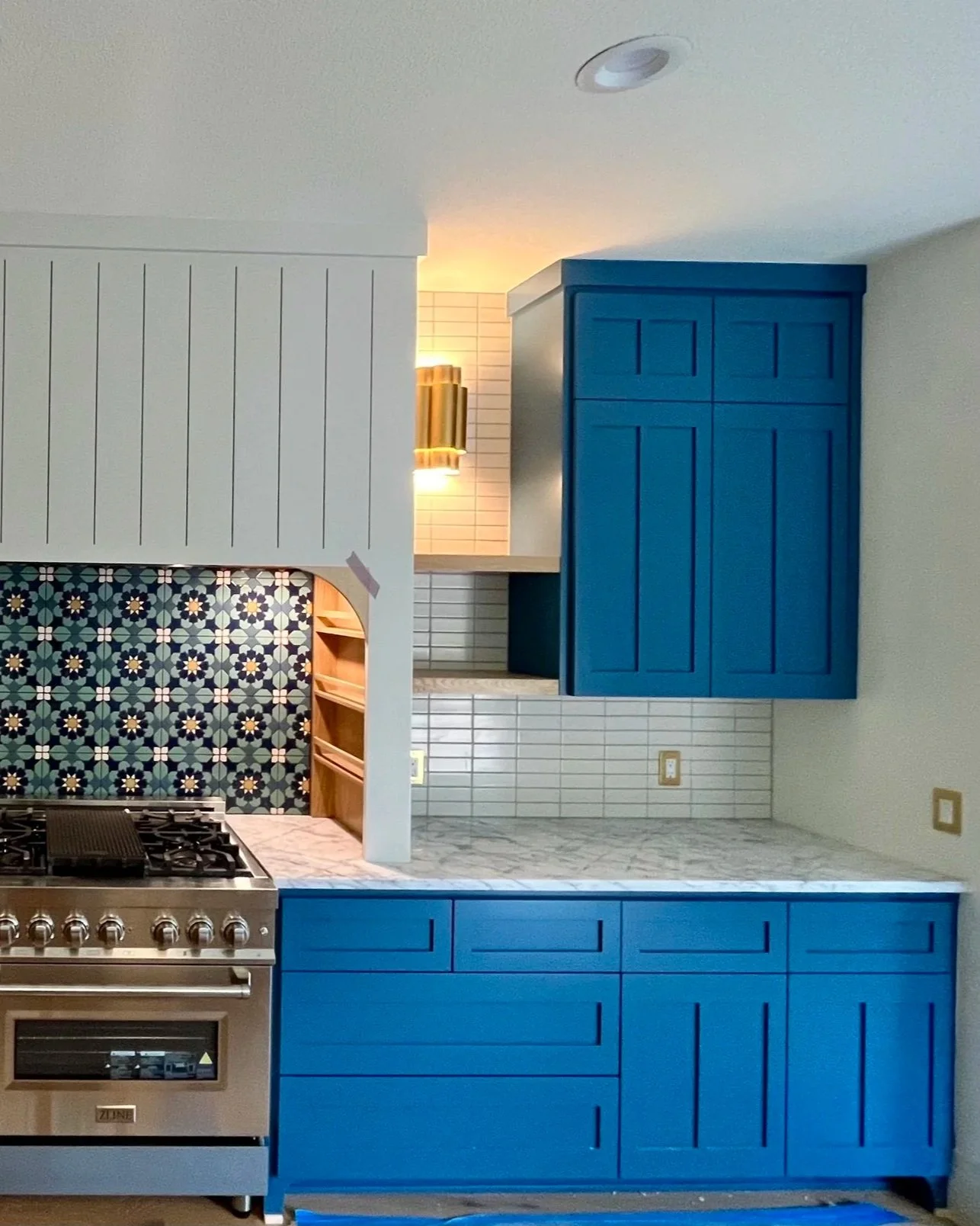 Kitchen with blue cabinets, marble countertop, white tile backsplash, and a stainless steel stove. A decorative tile wall with a pattern is visible in the background.