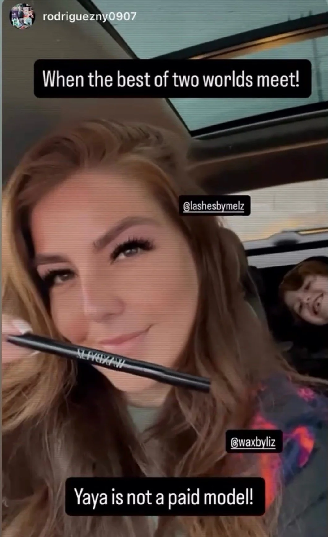 A woman with long wavy hair is smiling with makeup on her eyes and cheeks, holding a black makeup brush in her mouth. She is sitting in a car, with a ponytail hairstyle, and a boy with short hair is in the backseat, sticking out his tongue and smiling. The photo has text overlays saying "When the best of two worlds meet!", "Yaya is not a paid model!", and Instagram handles '@lashebymelz' and '@waxbyliz'.