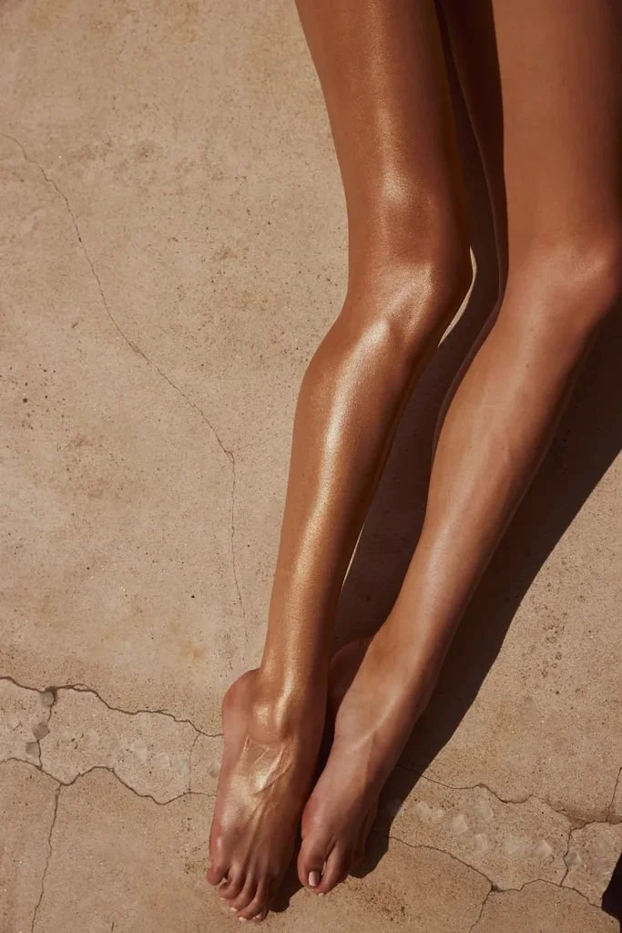 Two slender legs with shiny, tan skin lying on a cracked concrete surface, with feet close together.