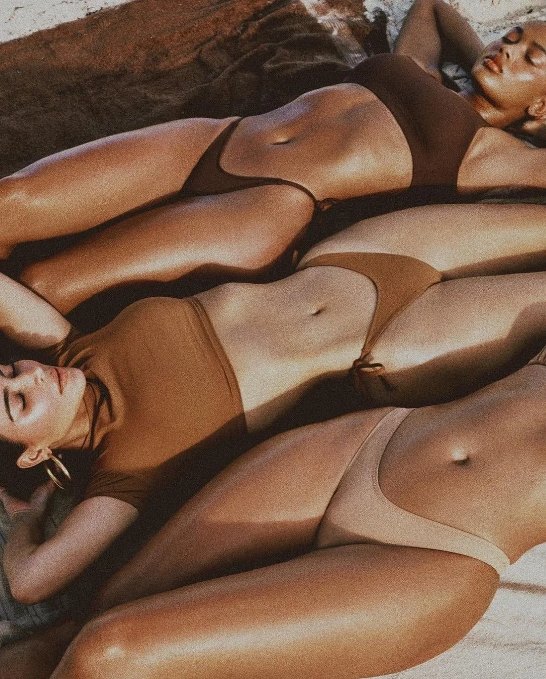 Women lying on their backs on the beach in bikinis showing their waxed, perfectly smooth skin, with sunlight or warm lighting reflecting on their skin.